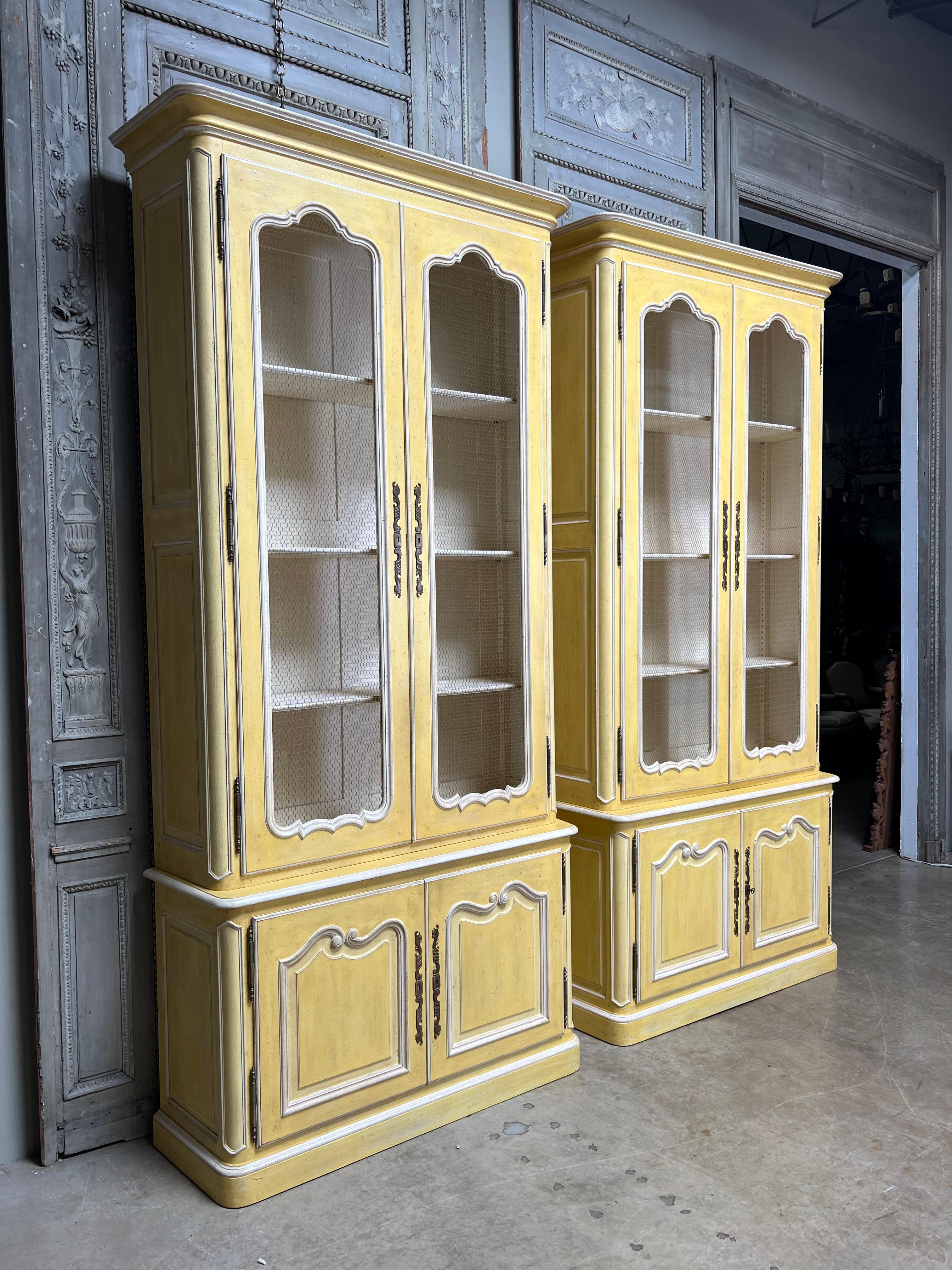 A large pair of French Louis XV style bookcases in a yellow and white painted finish.  These wonderful cabinets are handcrafted and hand carved, with peg construction.  They are very fine quality and highly decorative.  
The finish is a butter