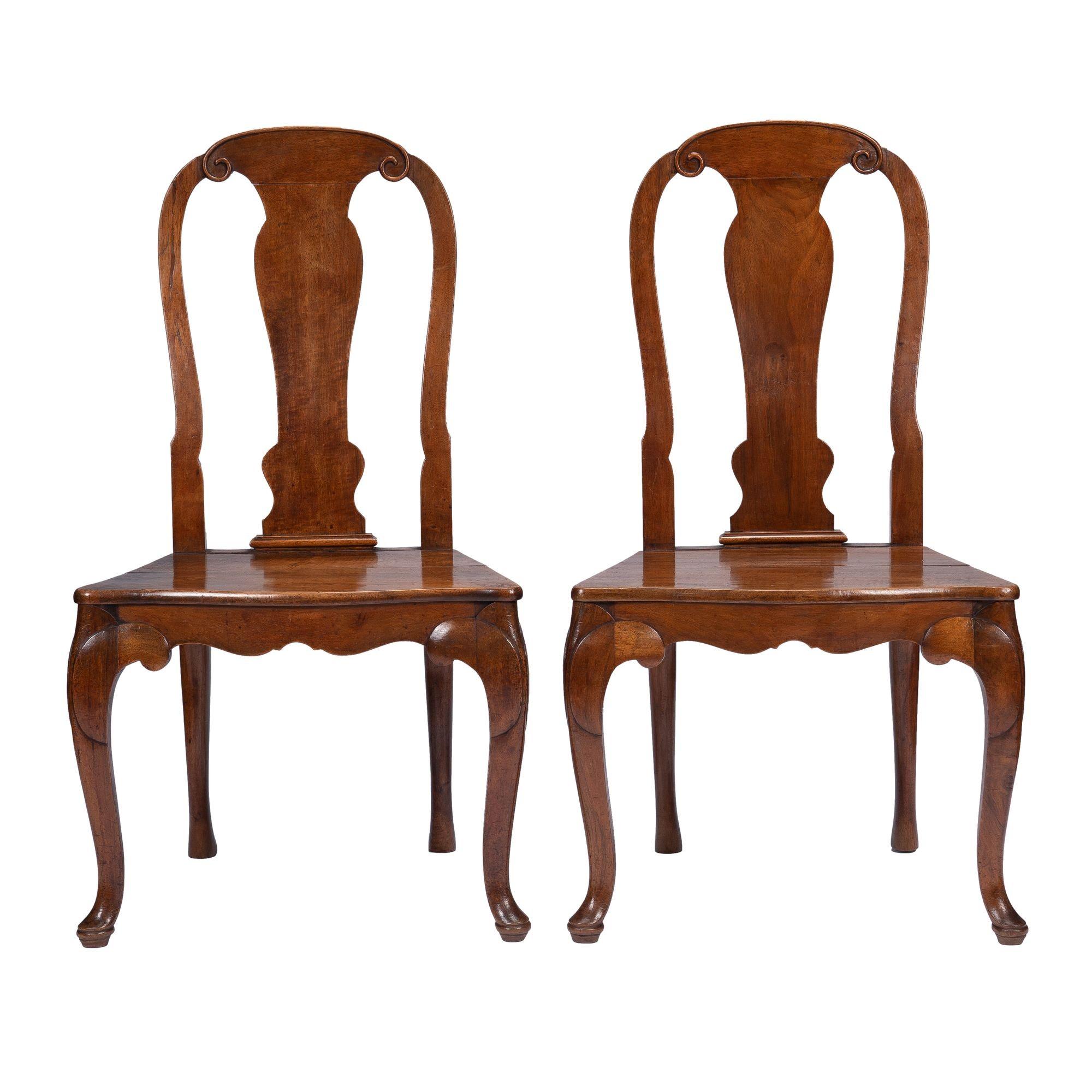Pair of French walnut plank seat hall chairs on cabriole legs in the Louis XV taste. The tall chair backs frame a shaped central back splat which terminate in a shoe at the base of the plank seat. The chairs are fitted with custom boxed seat
