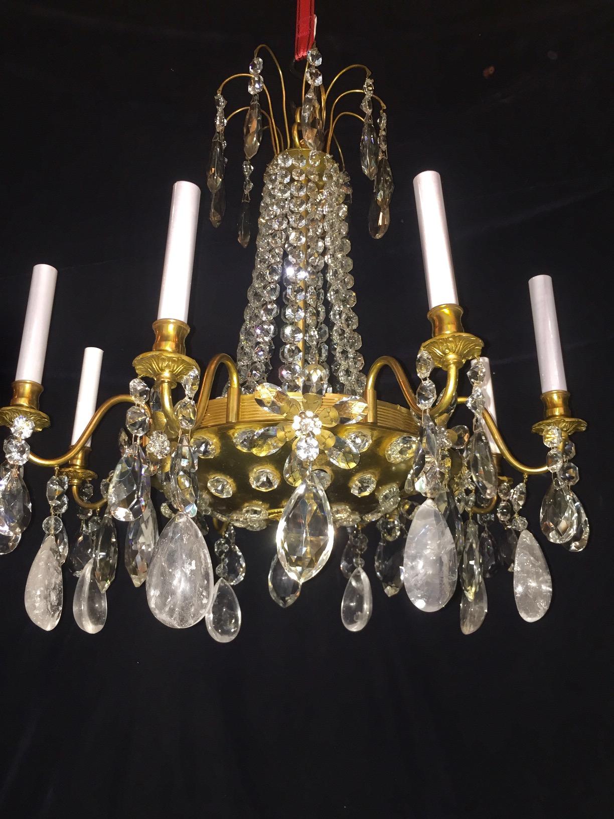 A pair of unusual antique French multi light gilt bronze, cut rock crystal and crystal chandeliers of fine detail embellished with rock crystal prisms, large crystal flowers and cut crystal chains further adorned with a central gilt bronze dish in