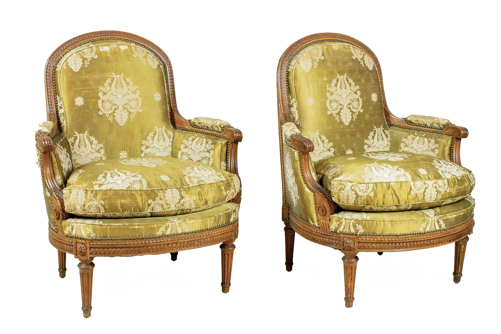 Paire de bergères / fauteuils Louis XVI (XVIIIe siècle) en bois de hêtre sculpté, avec bordure à motif de perles sculptées sur le dossier arqué et le cadre de l'assise, avec des bras sculptés d'acanthes et de volutes et une tapisserie en damas doré