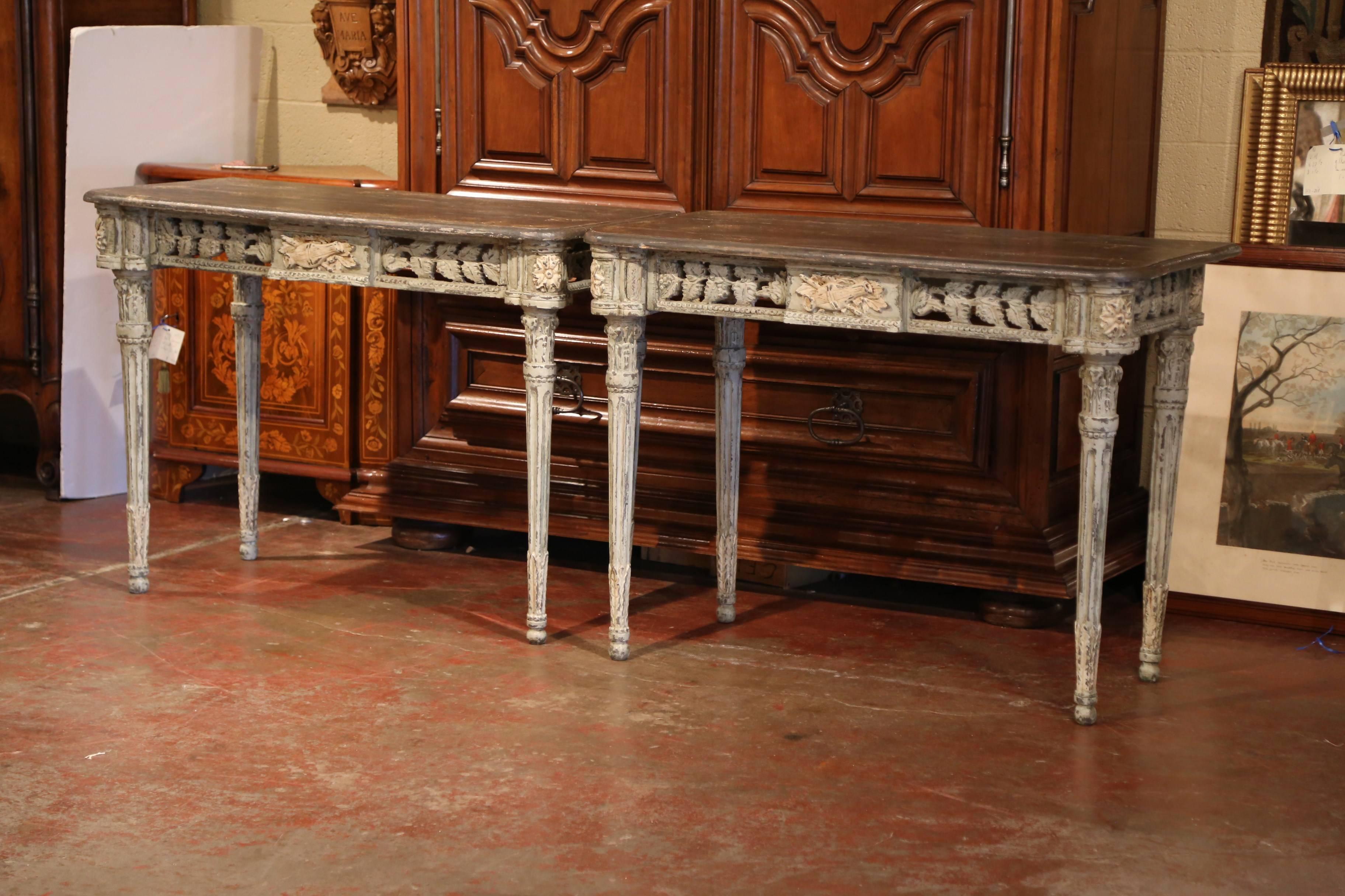 This elegant pair of antique, painted consoles was crafted in the southwest part of France using old elements. Each table features four tapered legs with acanthus leaves at the bottom, round corners with flowers medallions and delicate carvings