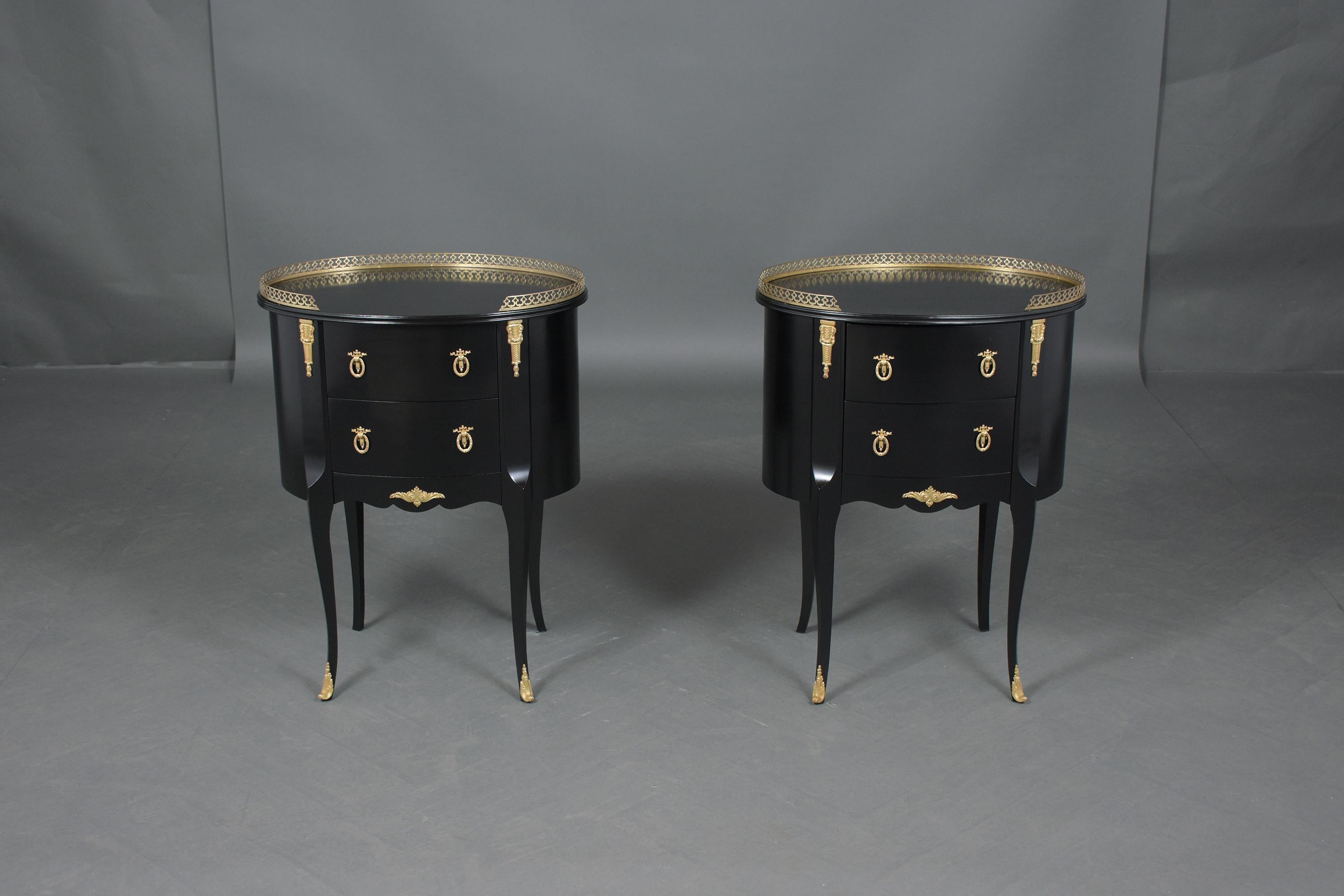 An extraordinary pair of early 1910s french commodes hand-crafted out of mahogany wood and this pair of side tables feature an elegant ebonized color with a lacquered finish. The oval shape tops have a brass gallery, and two pullout drawers each