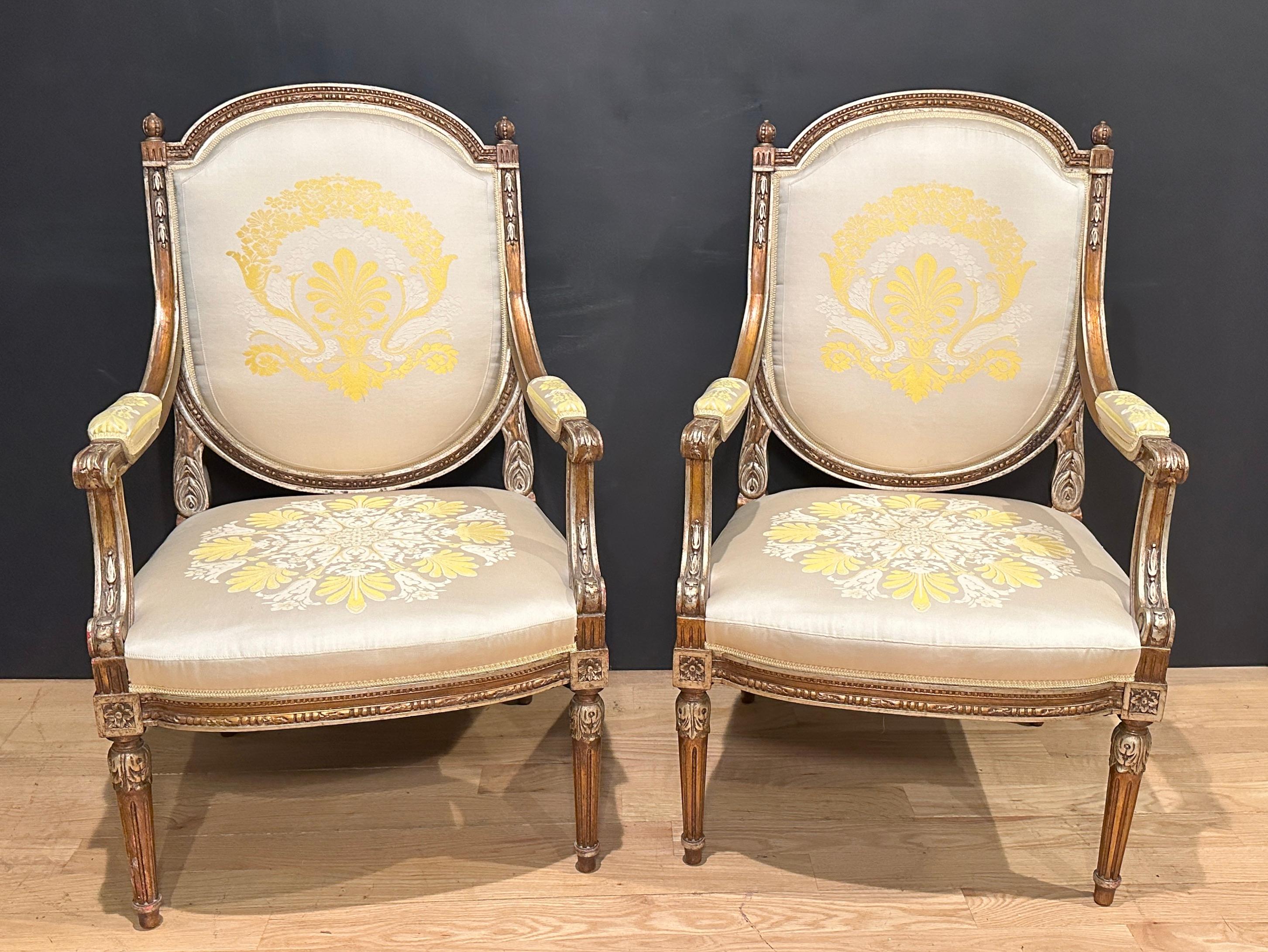 Fine pair of antique French Louis XVI style armchairs/fauteuils. Silver gilt details with a bronze tone gold ground. Upholstered in a champagne silk brocade with gold and ivory highlights.