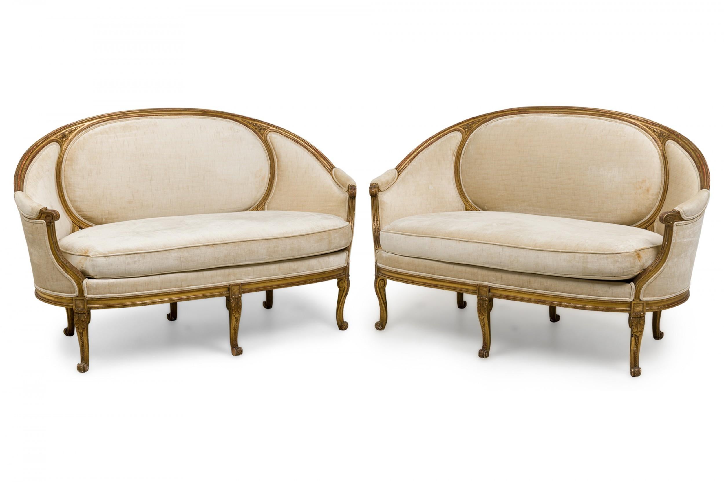 Pair of French Louis XVI (18th Century) canapes / settees with a curved and carved giltwood frame with a circular panel in the backrest, which curves forward to create the settee\'s arms, upholstered in a beige ribbed velvet, and resting on five