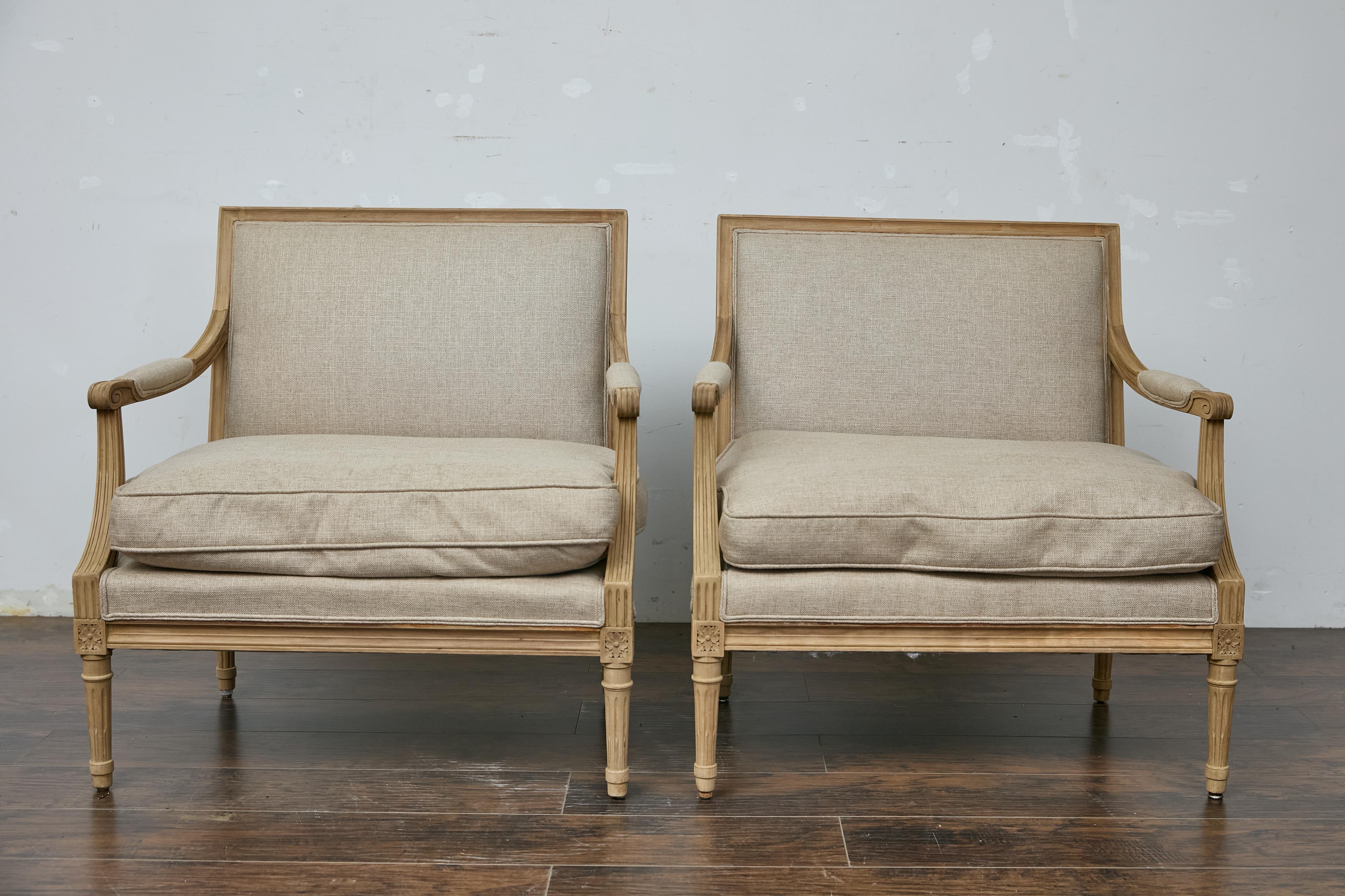 A pair of French Louis XVI style painted wood marquise chairs from circa 1920 with scrolling arms, fluted legs, carved rosettes and new custom upholstery. This elegant pair of French Louis XVI style marquise chairs from circa 1920 captures the