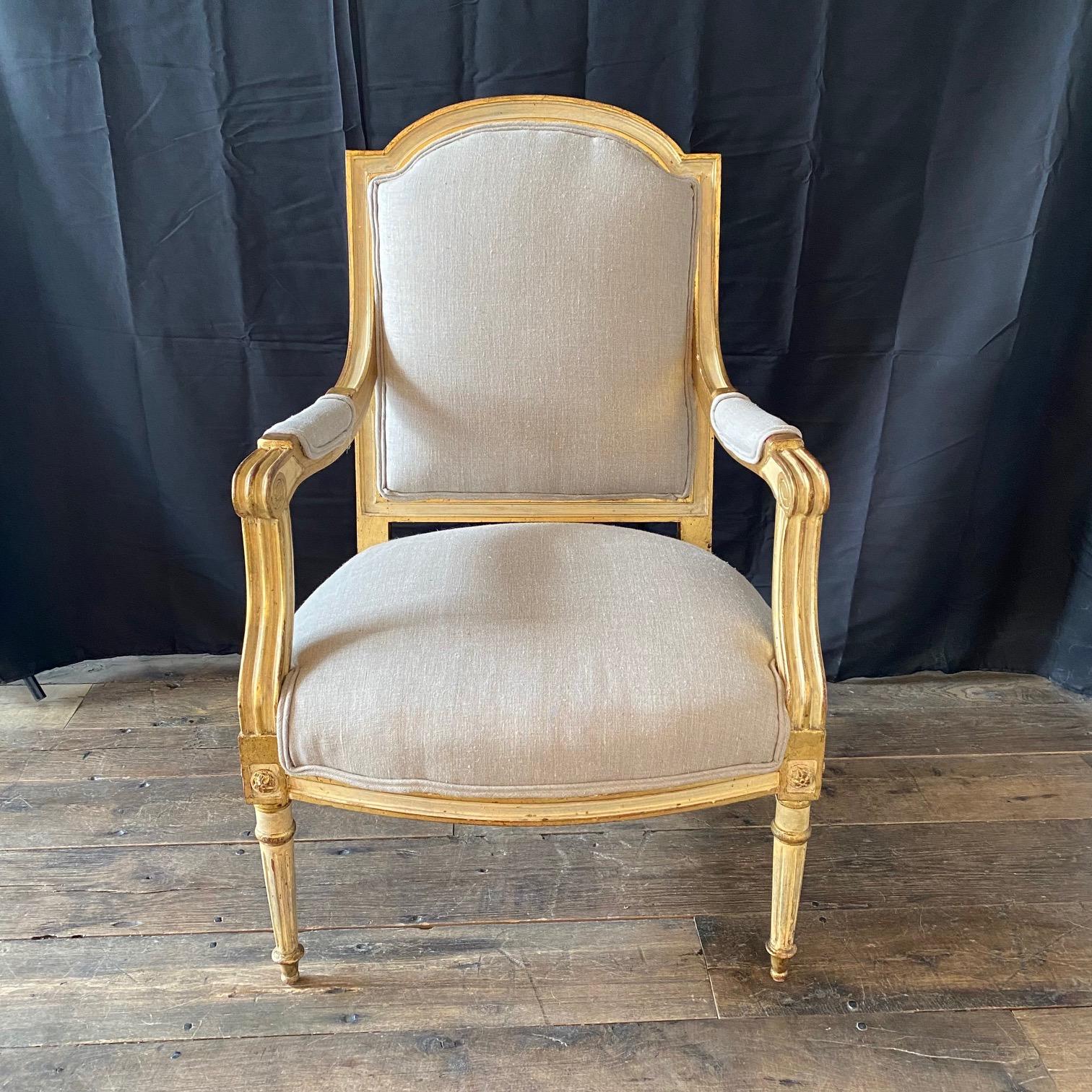 An elegant and very comfortable pair of French Neoclassical giltwood armchairs or fauteuils in the Louis XVI style, both frames showing arched crest-rails with upholstered backs, sided by padded armrests terminating to carved grips over generously