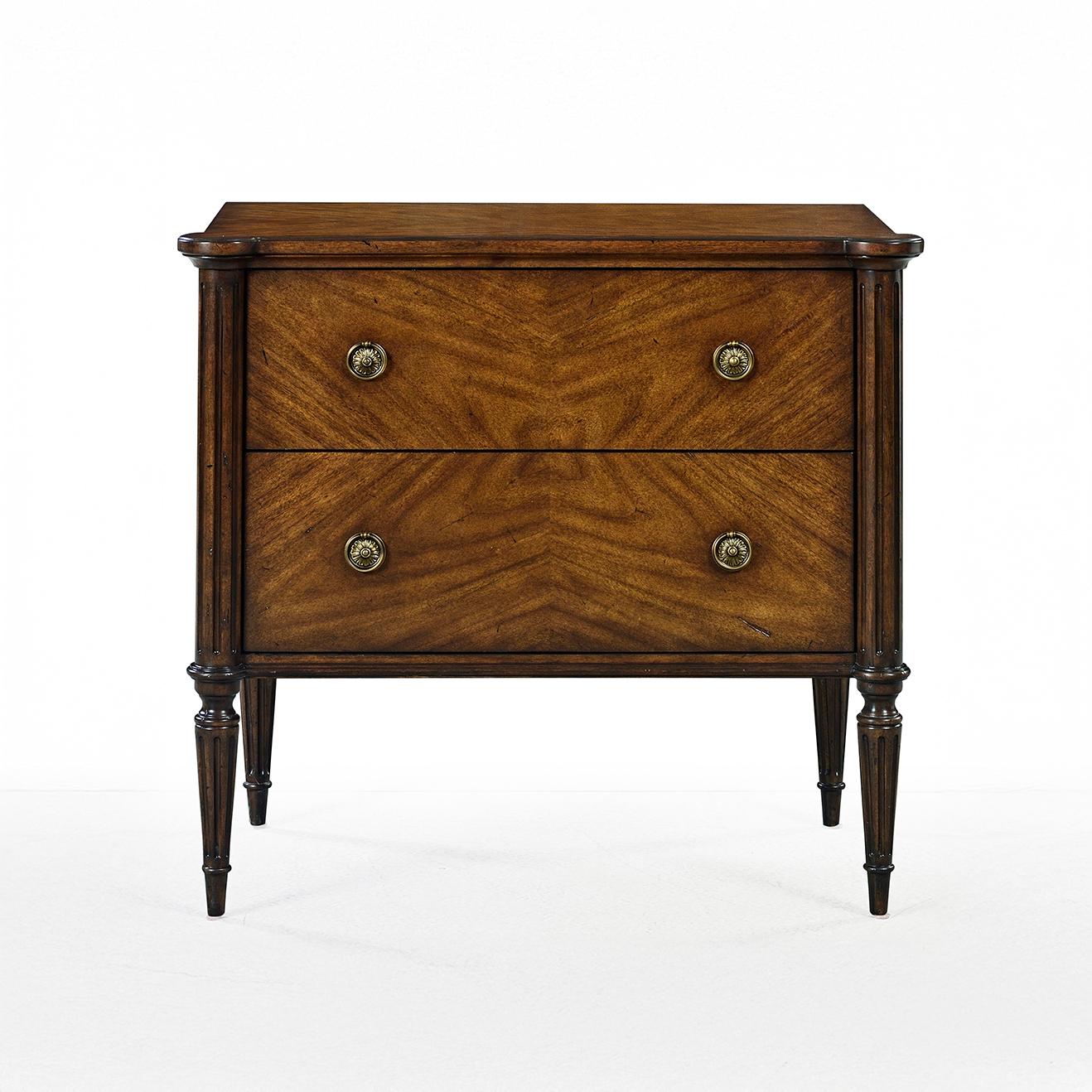 The nightstand captures the essence of neoclassical elegance in a compact and versatile form. Expertly crafted with a rich mahogany finish, this two-drawer chest showcases classic fluted, tapered legs, bookmatched drawer fronts, and traditional