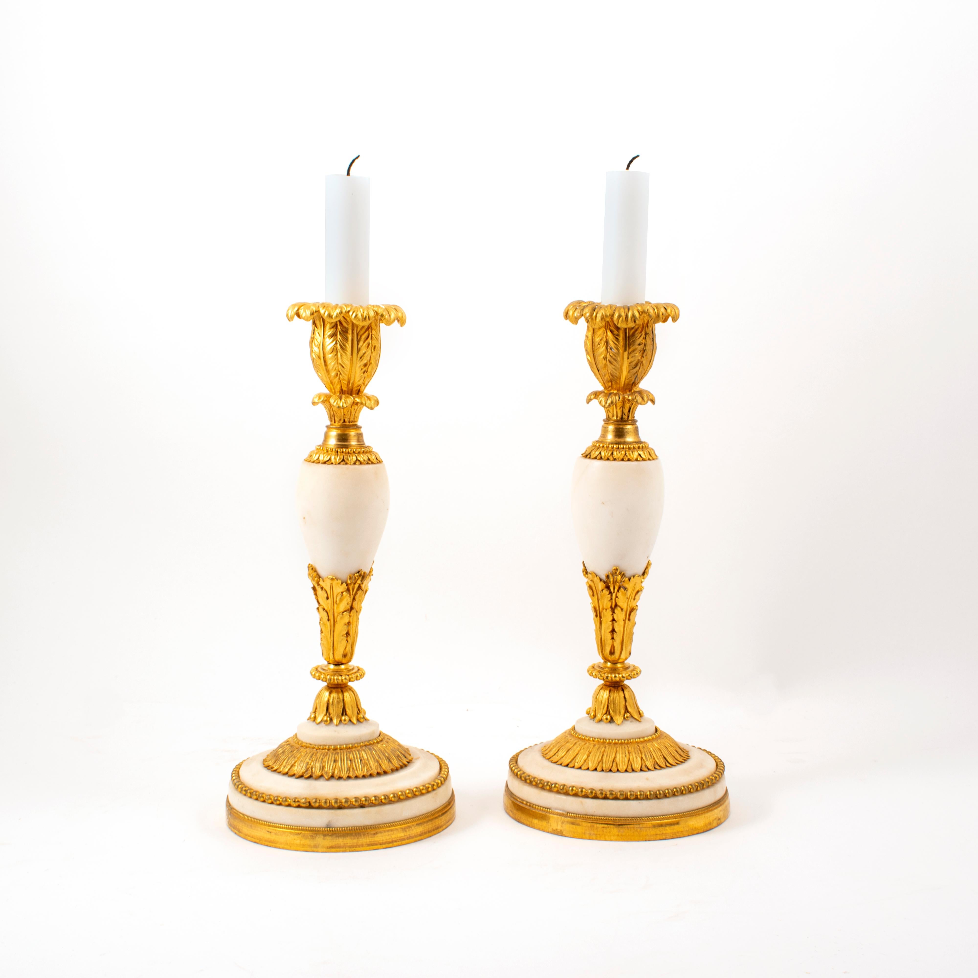 Pair of French Louis XVI ormolu and white marble candlesticks, late 18th century, with leaf tip bobeche, baluster form with leaf tips, raised on a circular pedestal base with ormolu banding.
France 1790-1800.