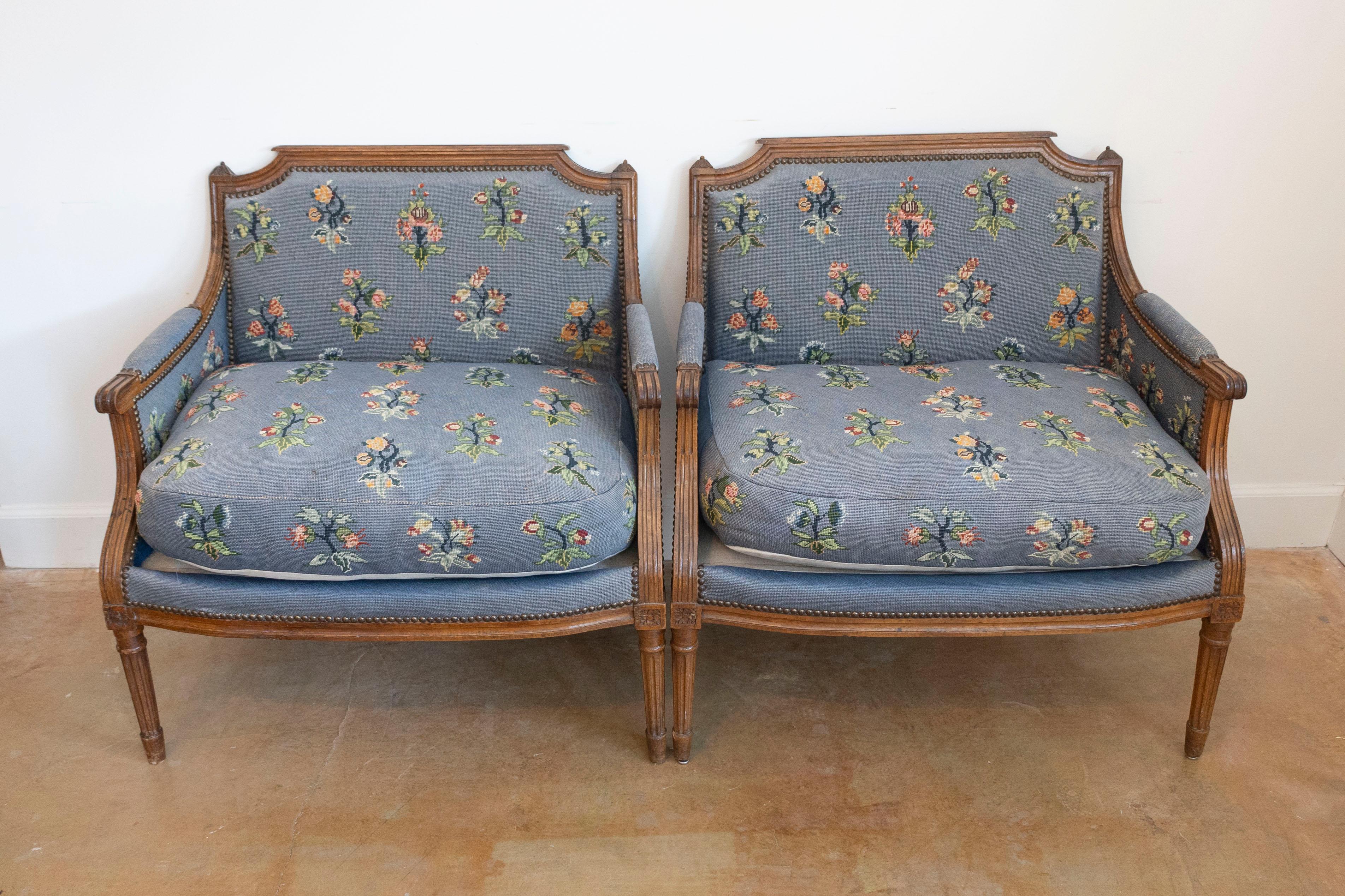 A pair of French Louis XVI period bergères marquises chairs from the late 18th century, with wide seats, carved rosettes, fluted legs and floral upholstery. Created in France during the last decade of the 18th century which saw the end of the