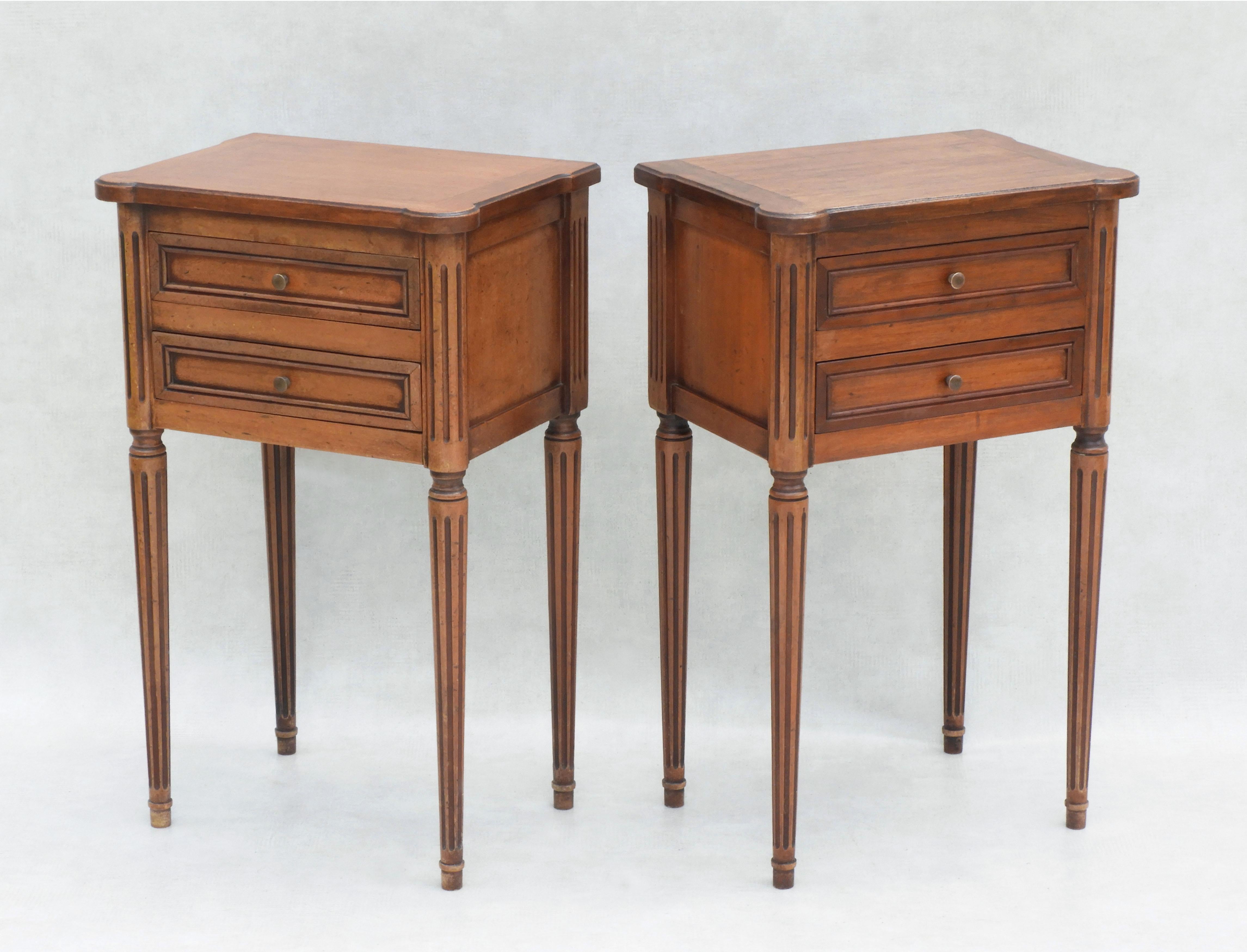 Two Midcentury Louis XVI Revival bedside tables or nightstands.
A Duo of Neoclassical-style two-drawer walnut side cabinets with carved fluted tapered legs and column detailing and brass handles. Stylish and practical tables that will work equally