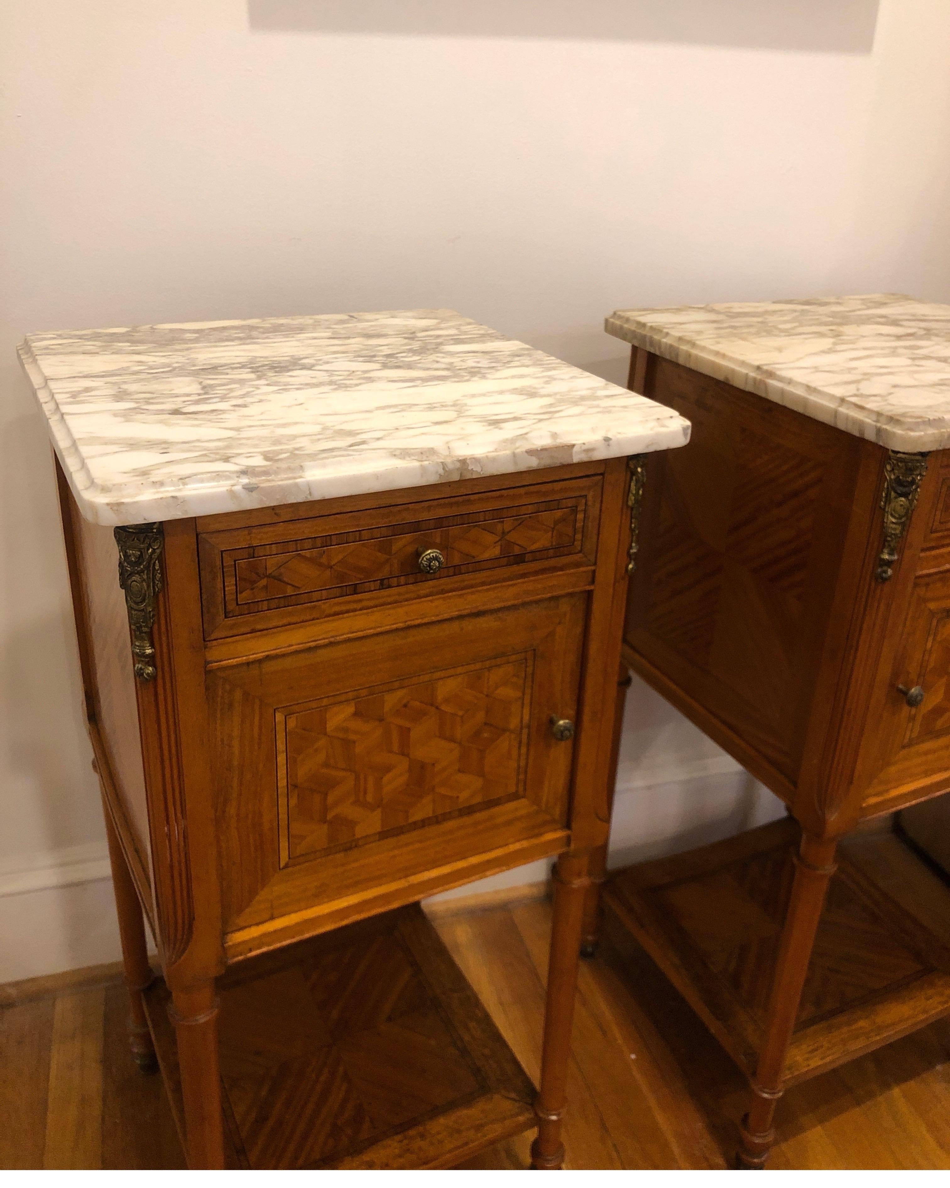 Pair of elegant French Marquetry side tables with gilt ormolu details. 
Doors open with original porcelain insert (please note, one piece of porcelain has damage).

Drawers and doors open smoothly. Marble tops remove for moving. Show signs of