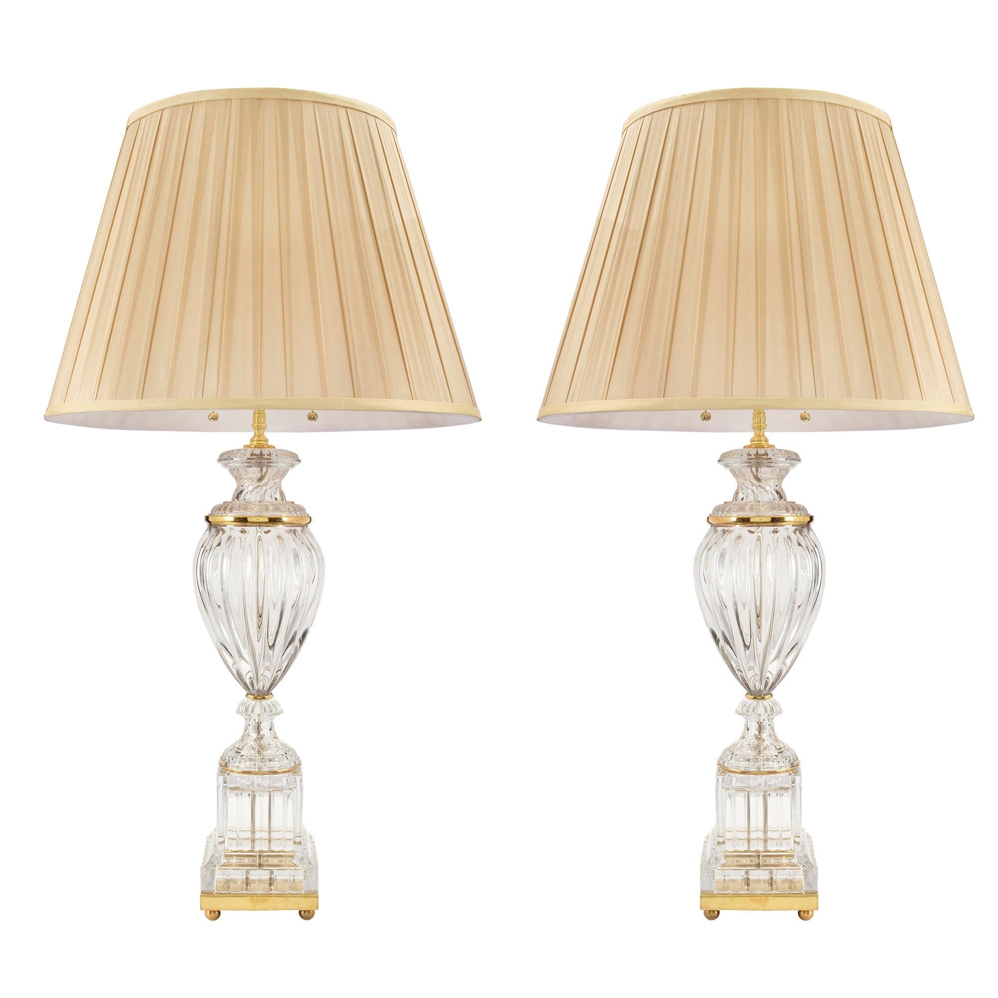 A pair of stunning and very elegant French Louis XVI style Baccarat style crystal and ormolu lamps. Each lamp is raised on ormolu ball feet below the ormolu support. At the bottom is a square cut base at rectangular column. Above is a baluster