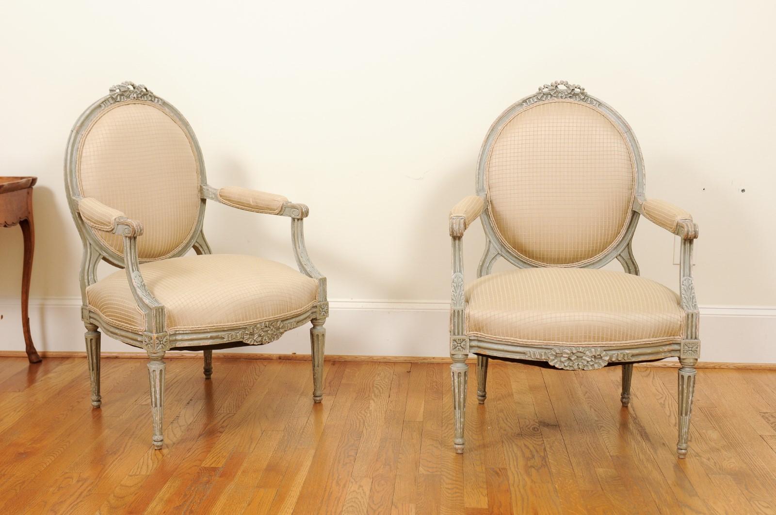 A pair of French Louis XVI style painted oval back armchairs from the mid-19th century, with carved ribbons and fluted legs. Created in France at the beginning of Emperor Napoléon III's reign, this pair of armchairs showcases the stylistic