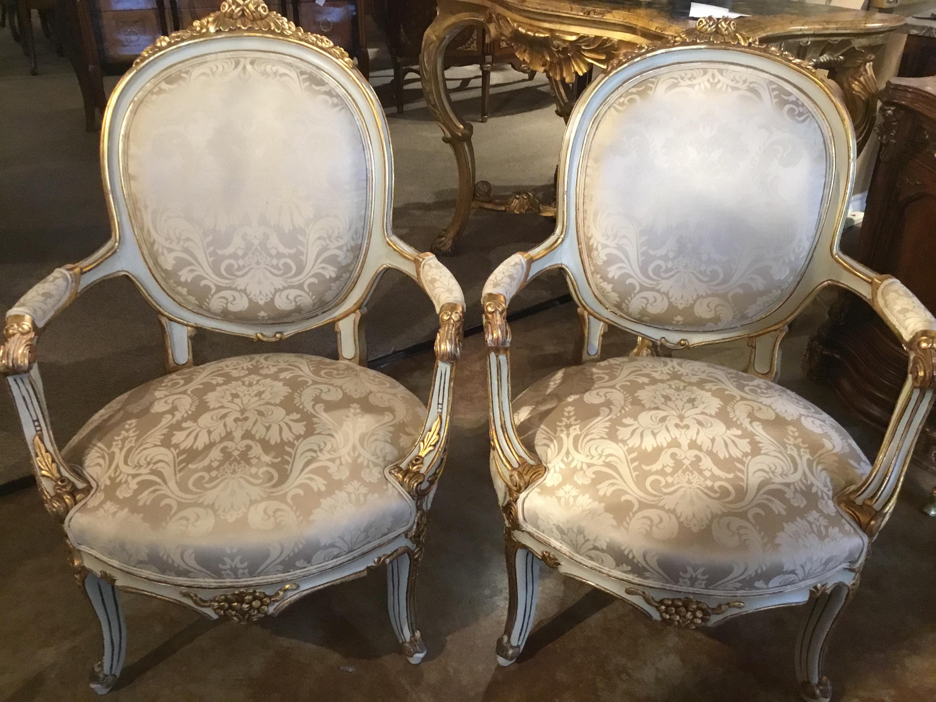 Pair of antique French parcel paint and parcel giltwood chairs with cream
Damask fabric. Carved gilt embellishments at the crest of roses and foliate
designs. The paint is a cream color.