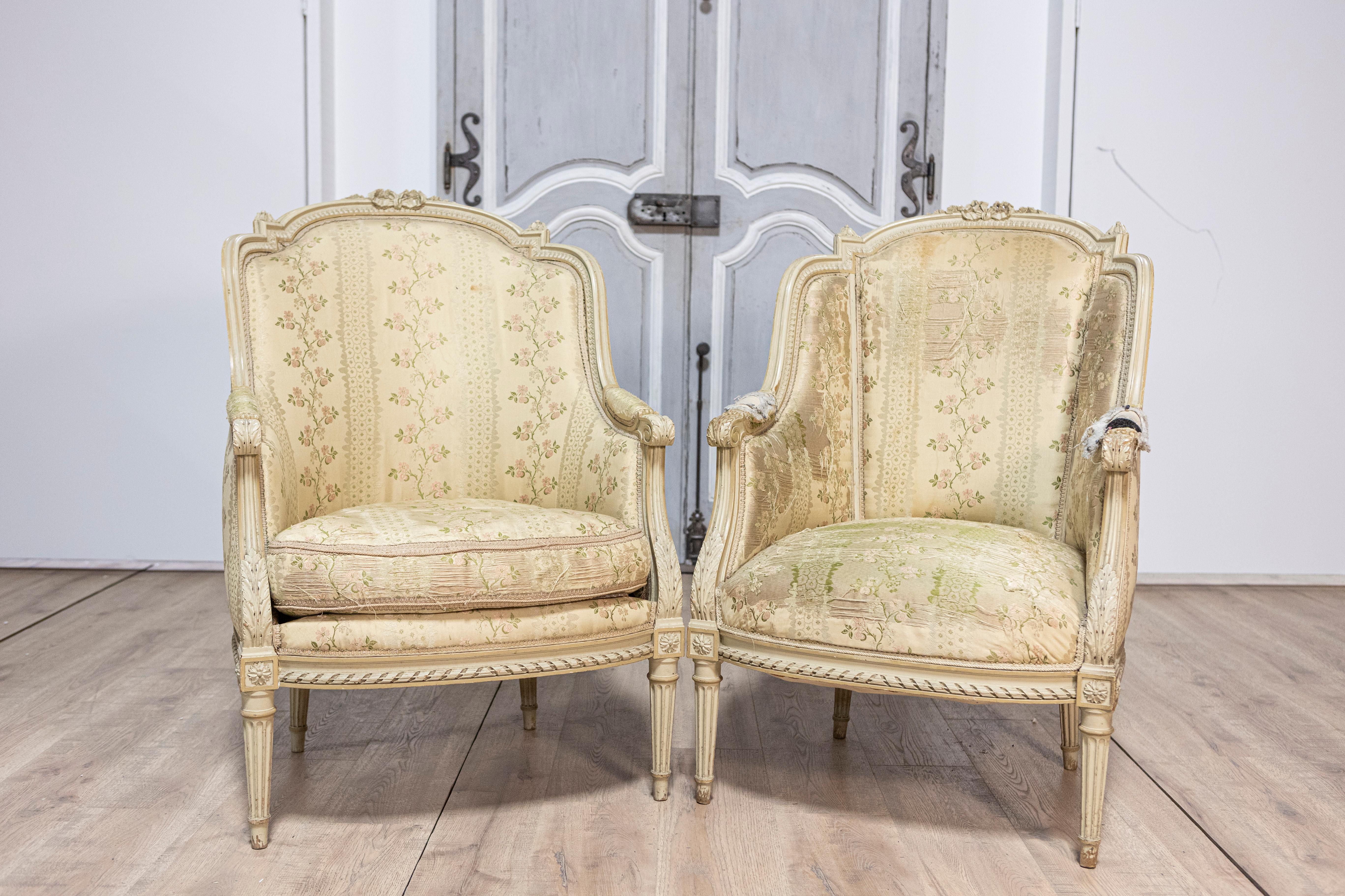 Pareja de bergères à oreilles francesas pintadas, estilo Luis XVI, de hacia 1900, con hojas de acanto talladas y patas estriadas. Esta exquisita pareja de bergères à oreilles francesas pintadas al estilo Luis XVI, de hacia 1900, presentan un acabado