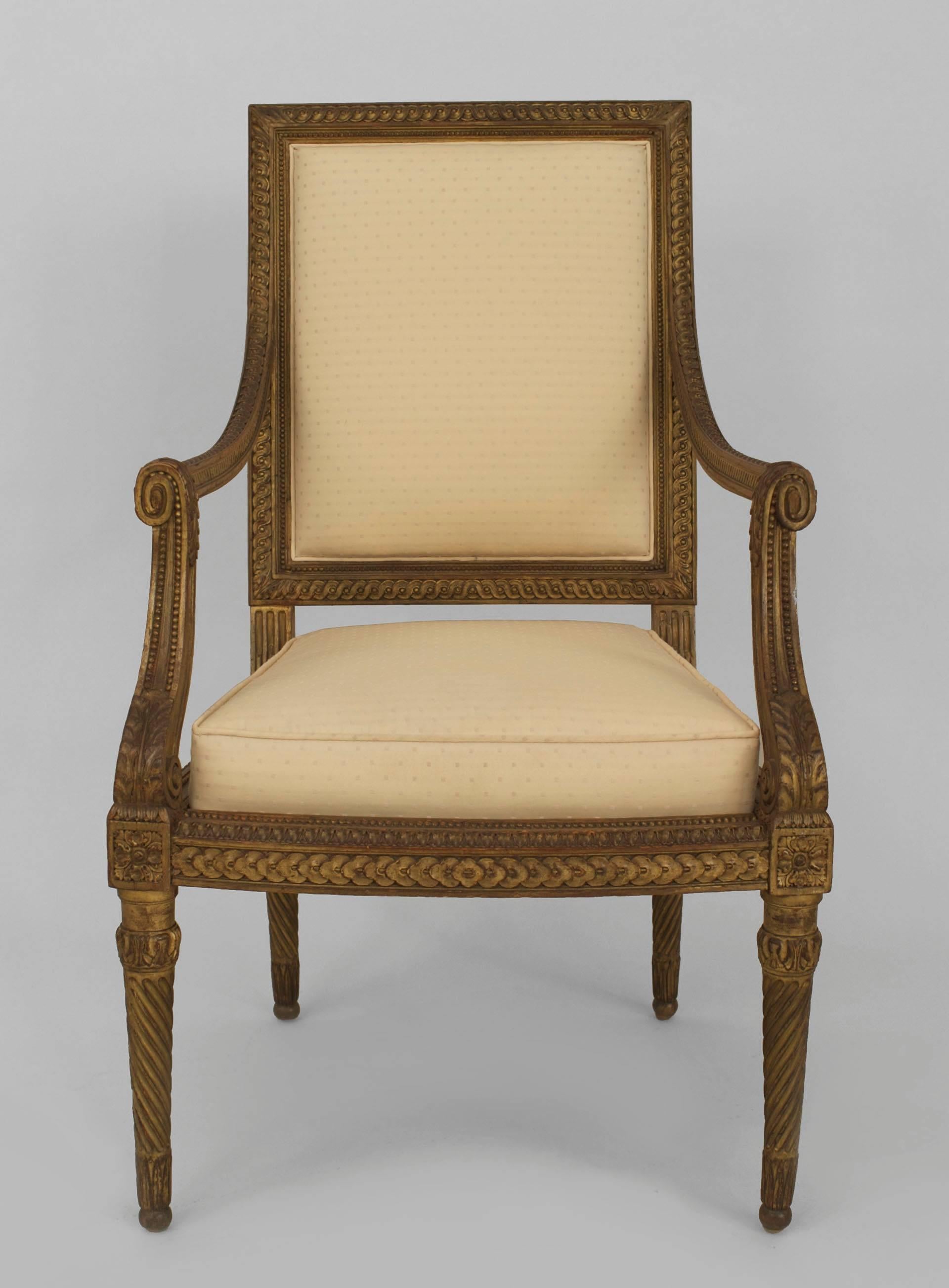 Pair of French Louis XVI style (19th century) gilt open armchairs with a carved frame on swirl form tapered legs with a light beige fabric upholstered back and box form seat.
   