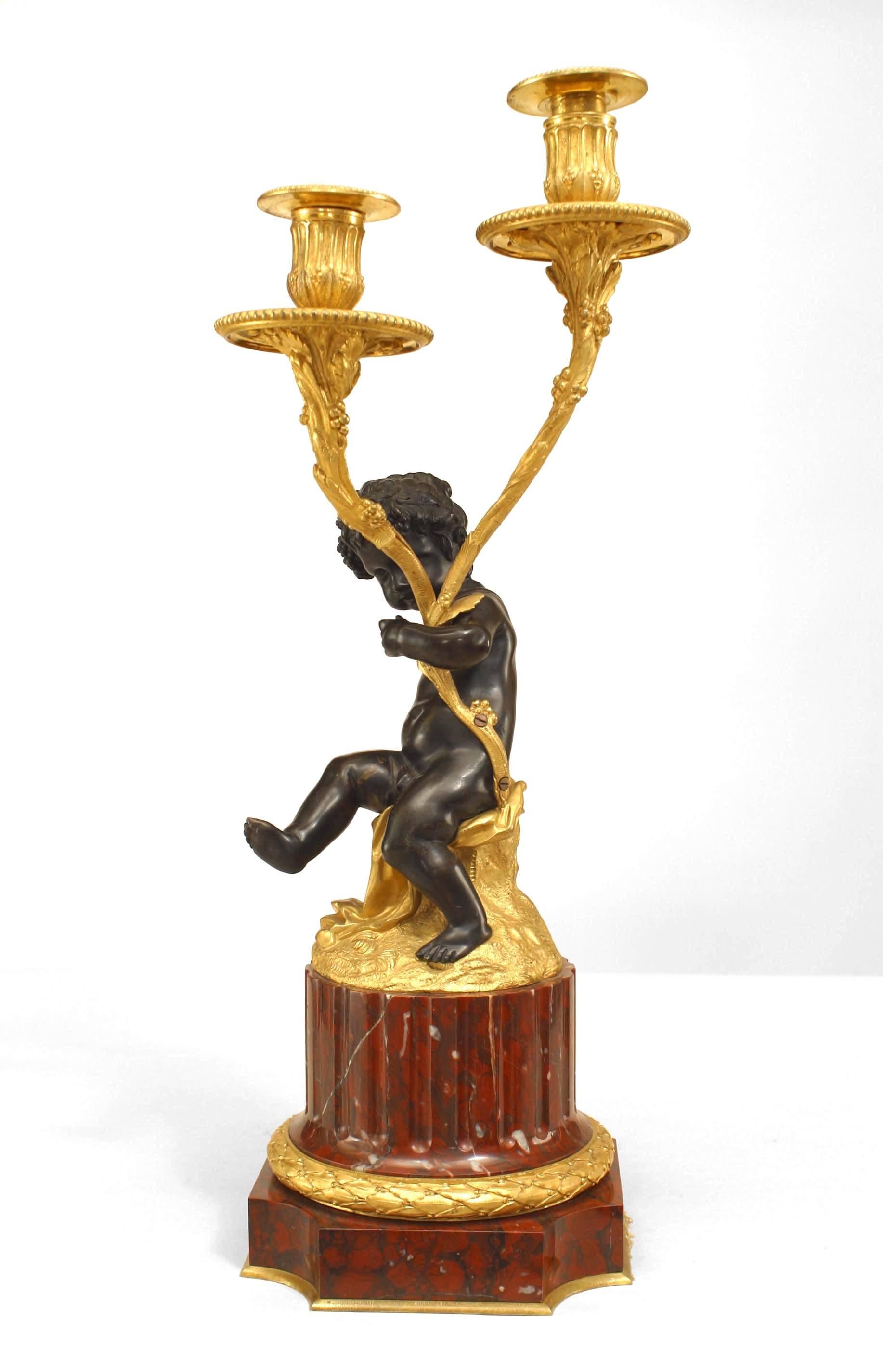 Pair of French Louis XVI-style (19th Century) gilt and patinated bronze candelabra with a cupid/satyr figure holding 2 foliate arms and raised on rouge marble bases (PRICED AS Pair)
