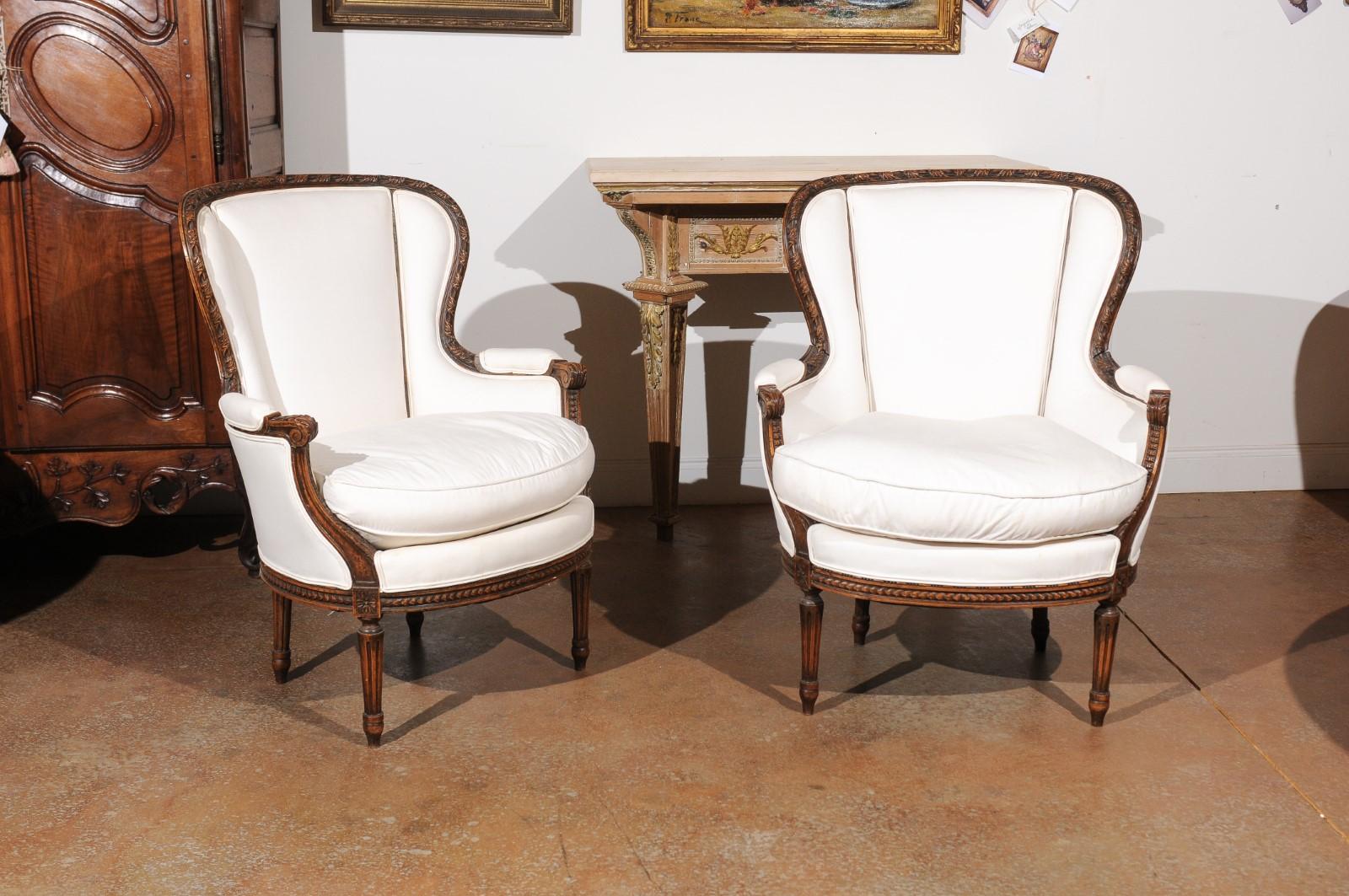 A pair of French Louis XVI style carved walnut bergères from the 19th century, with fan-shaped wingbacks and new upholstery. Born in France during the politically dynamic 19th century, each of this pair of bergère chair features a fan-shaped