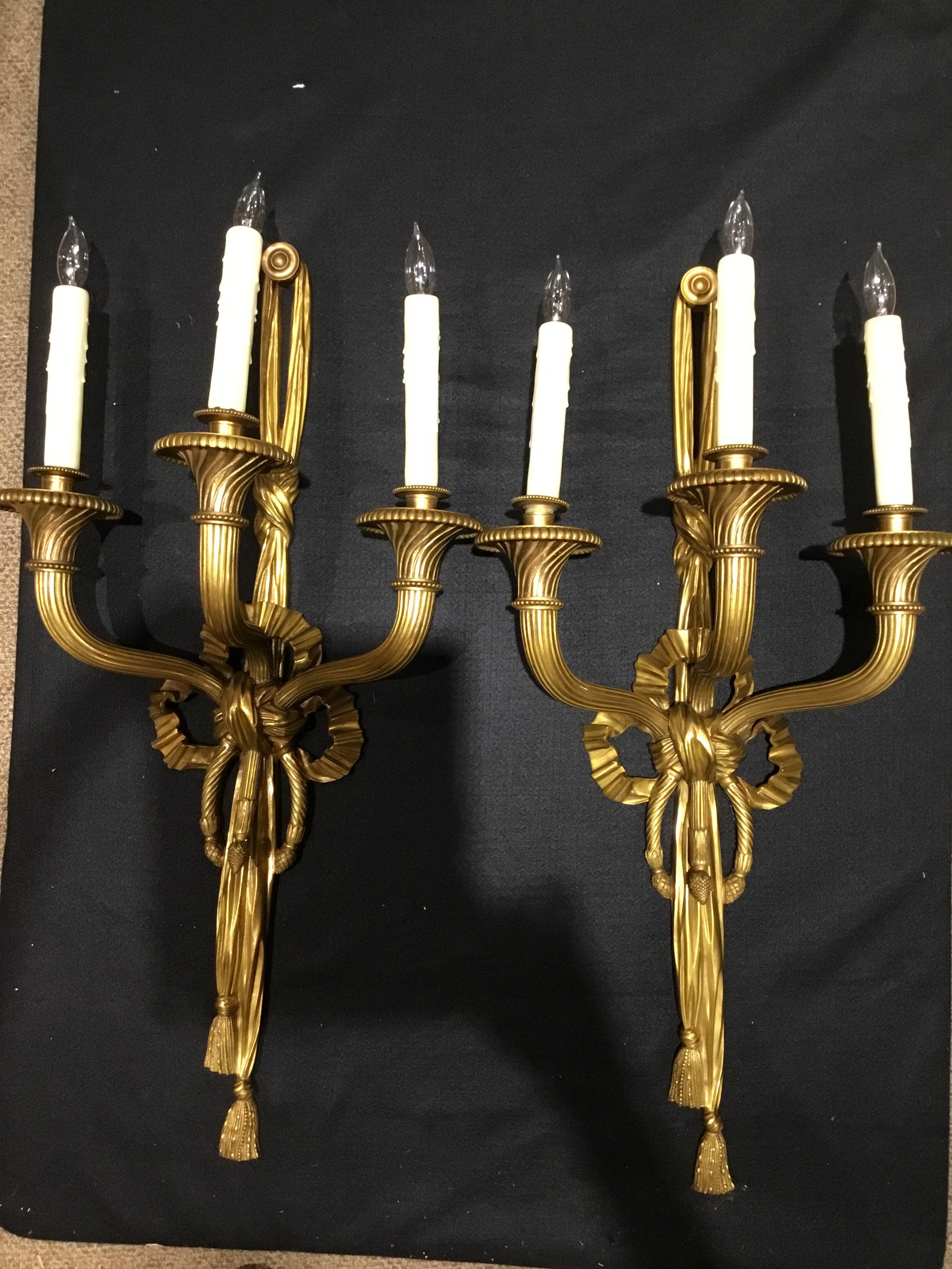 Pair of large and beautiful wall sconces that are wired with three lights,
Each having fluted arms extending from a ribbon form standard, ending
In bobéches with faux candle lights, 20th century.