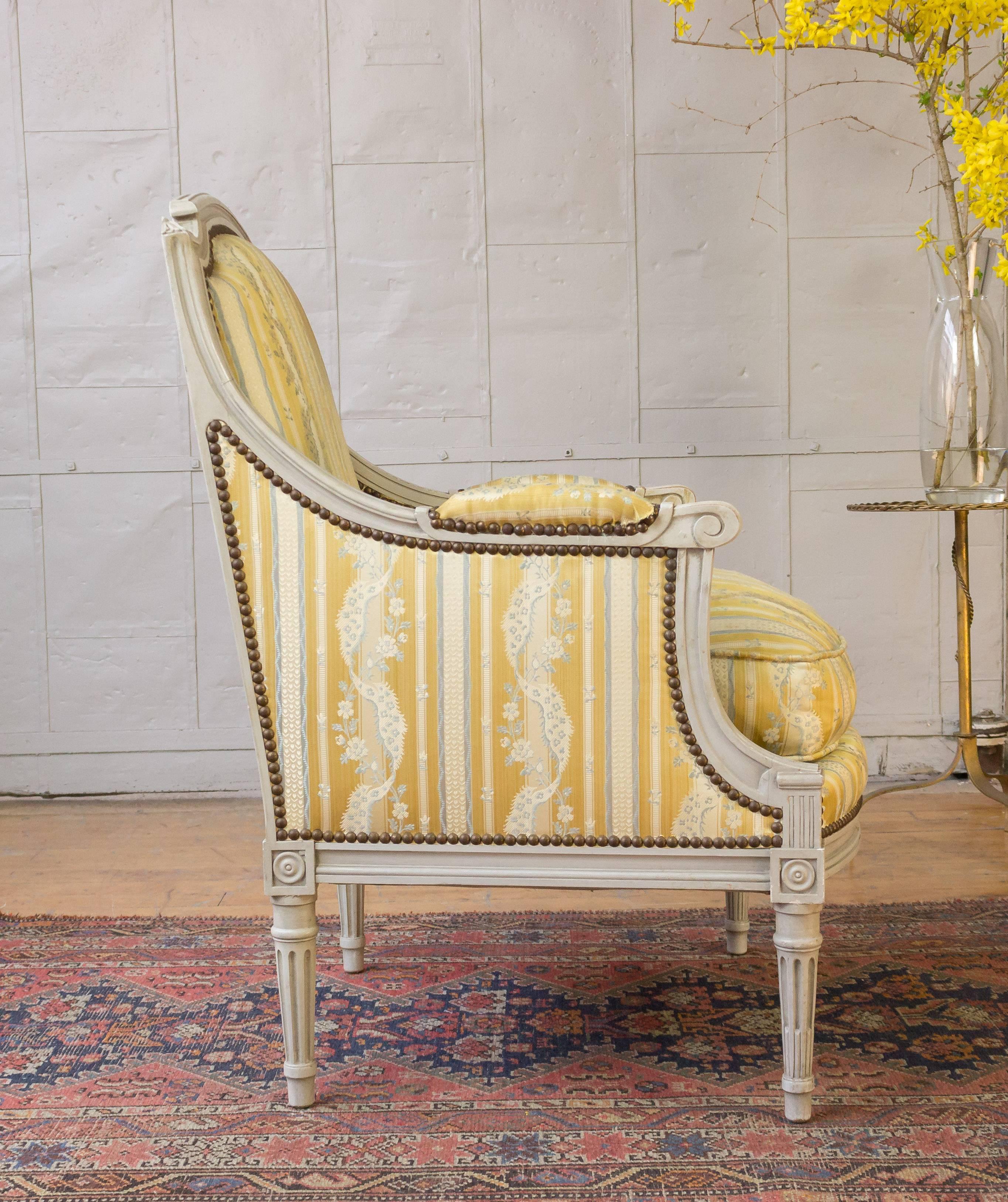 A sophisticated pair of French Louis XVI style armchairs. This exquisite pair of French Louis XVI armchairs will make a stunning addition to any home. Featuring graceful grey patinated and carved wooden frames, these chairs are classically designed