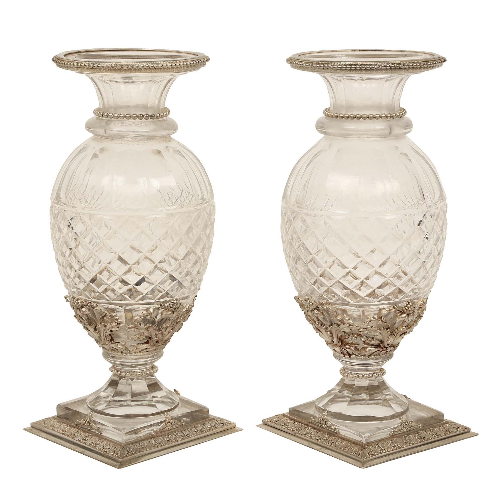 An elegant pair of French Louis XVI st. Baccarat cut crystal and silvered bronze vases. Each vase is raised by a chased square silvered bronze base decorated by chased acanthus leaves below the crystal socle pedestal. The square cut crystal body is