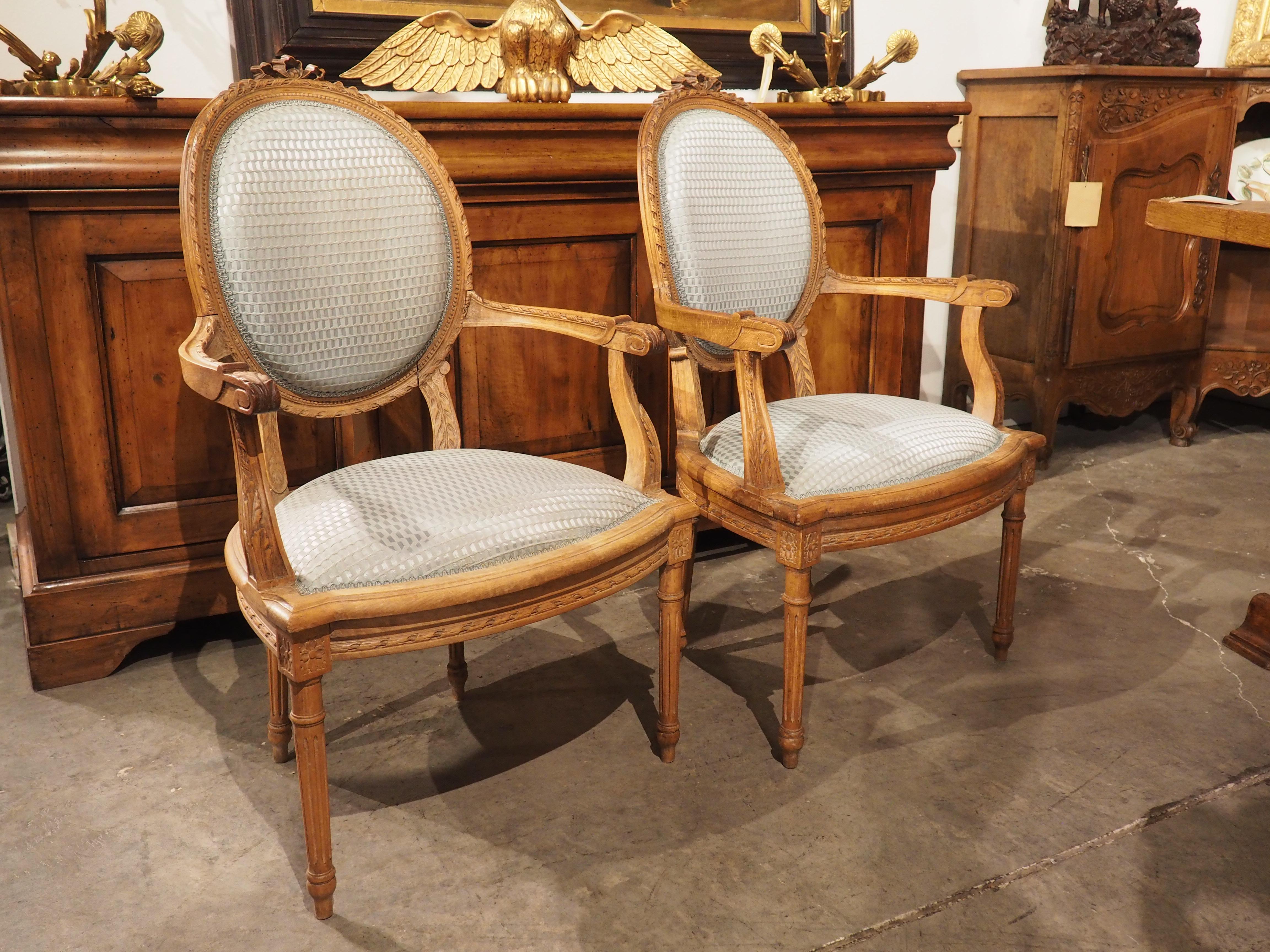 Hand-carved during the early- to mid-1900’s, this pair of French Louis XVI style armchairs has beautiful blue silk upholstery on the seats and back rests. The upholstery has a moiré rippled pattern and a matching sky blue gimp border on each