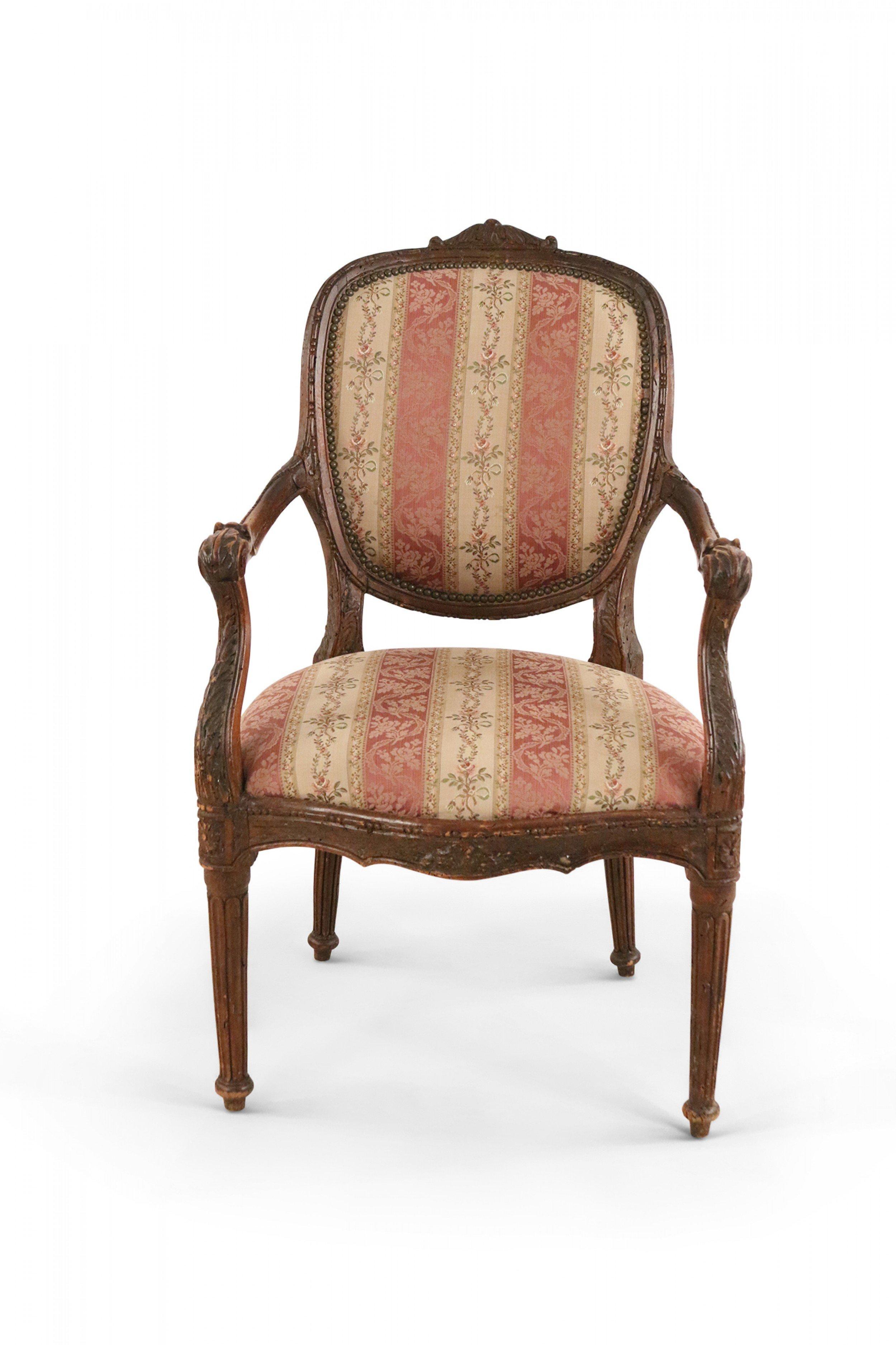 Pair of French Louis XVI walnut armchairs with beige and pink stripe upholstered oval backs and seats and carved foliate details along frame supported on fluted legs. (PRICED AS PAIR).
 