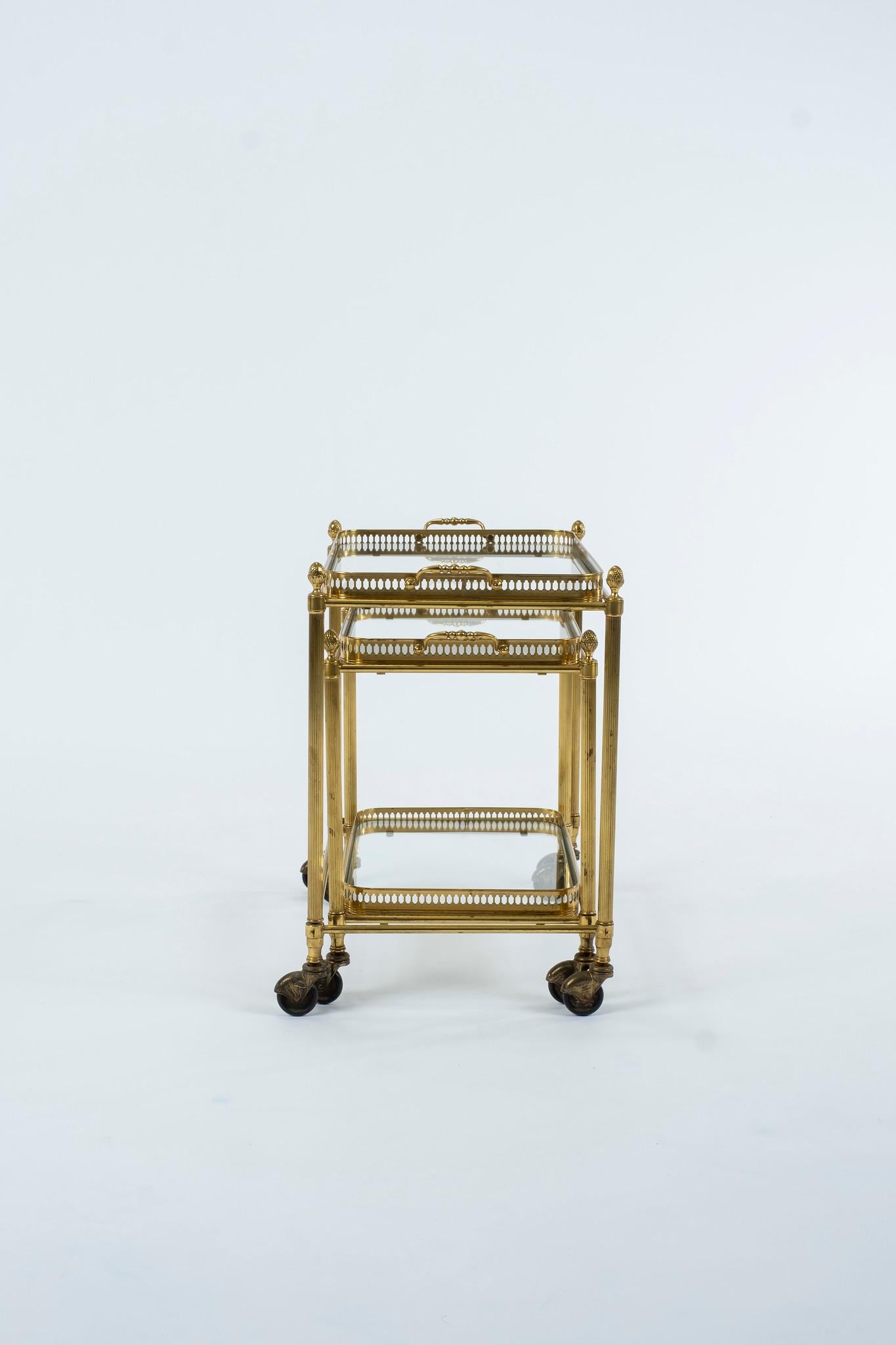 A vintage pair of French Louis XVI style brass nesting tables on casters with removable glass tray tops. These tables would work wonderfully as low lying bar carts.