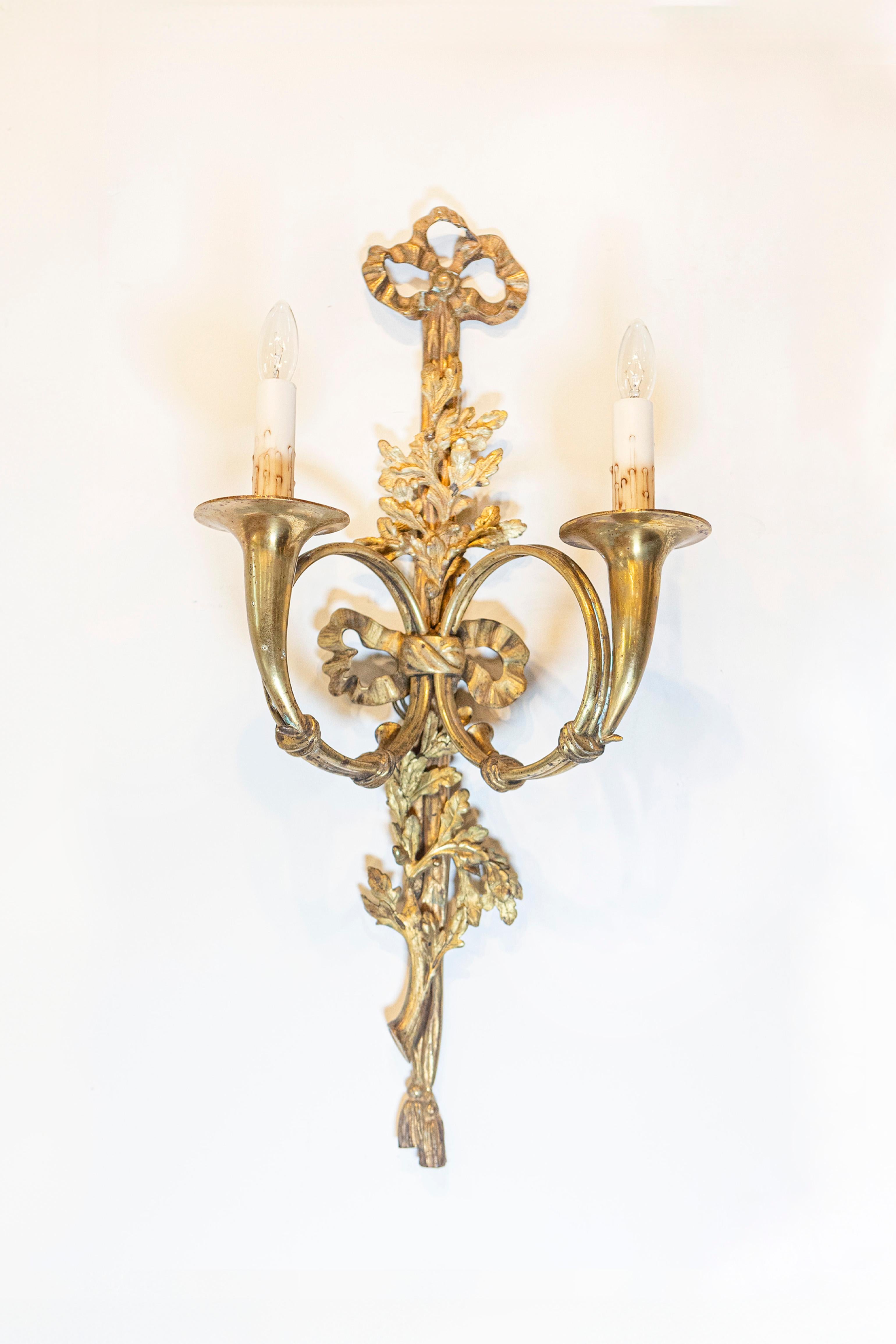 Coppia di appliques a due luci in bronzo in stile Luigi XVI del XIX secolo con nastri legati, motivi a fogliame e bracci in corno da caccia. Questa coppia di appliques francesi in bronzo presenta uno squisito decoro in stile Luigi XVI,
