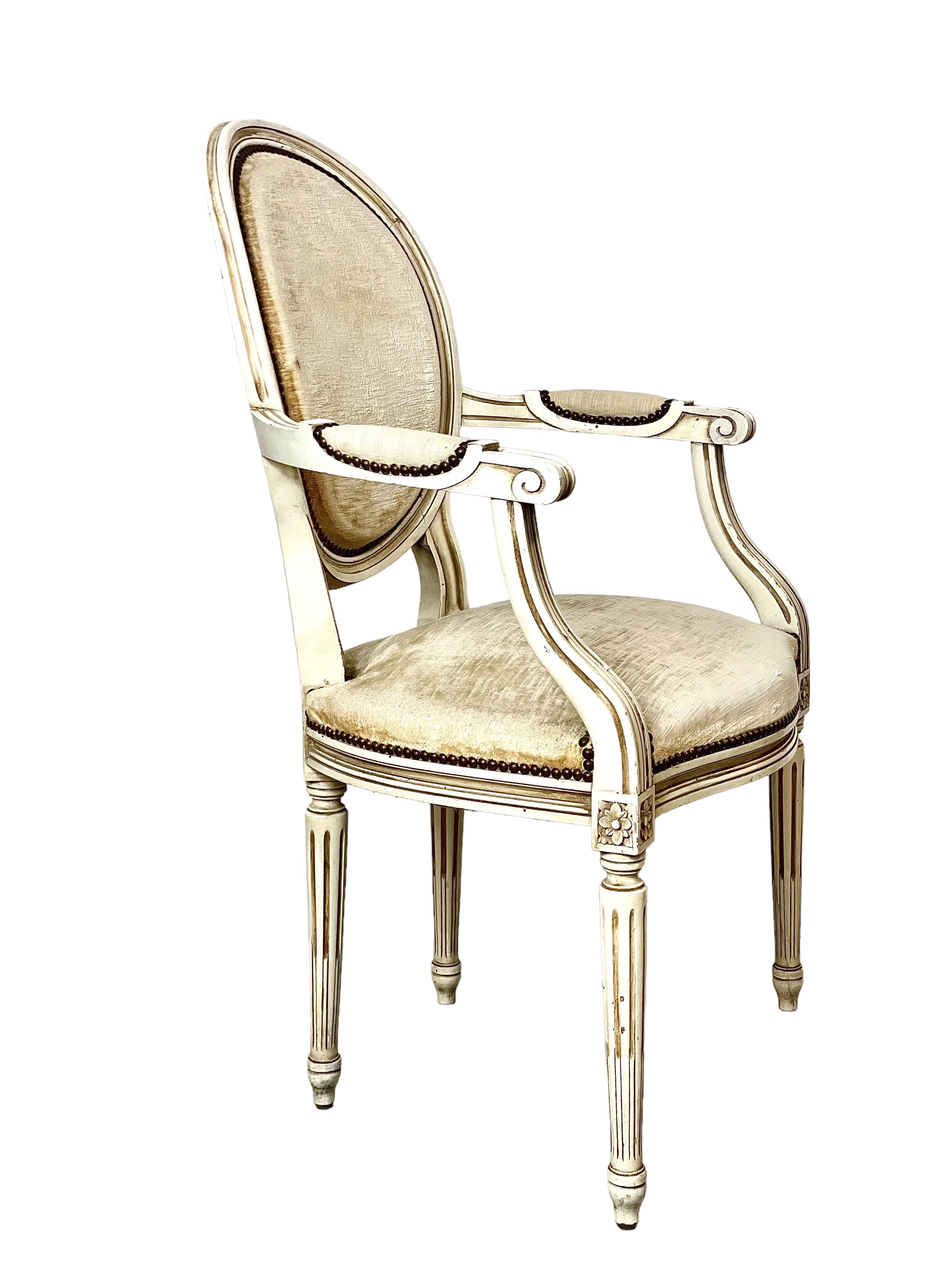 A pair of medallion-backed Louis XVI-style 'Fauteuil Cabriolet' armchairs, in white lacquered wood, and upholstered in creamy velvet. These chairs are wonderfully aged, with an authentic patina, and have the comfortable curved back of the classic