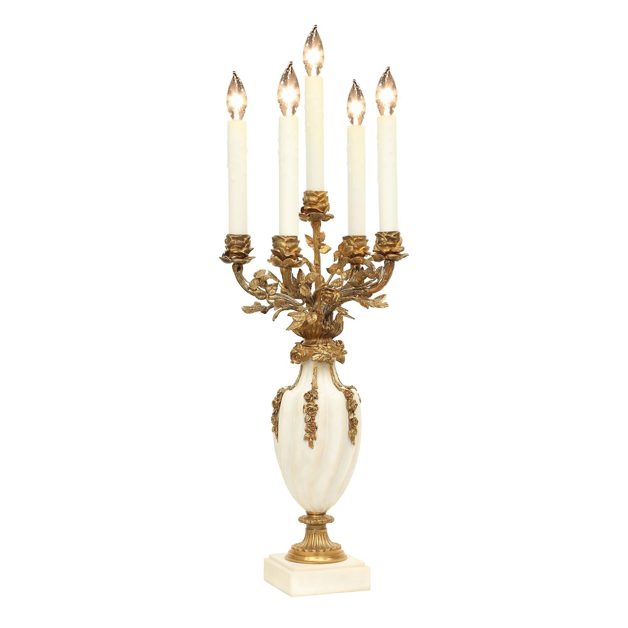 An elegant pair of French Louis XVI st. white Carrara marble and richly chased ormolu five-arm candelabras mounted into lamps. The pair is raised by a square base below an ormolu fluted base, supporting a spiral fluted design urn with floral ormolu
