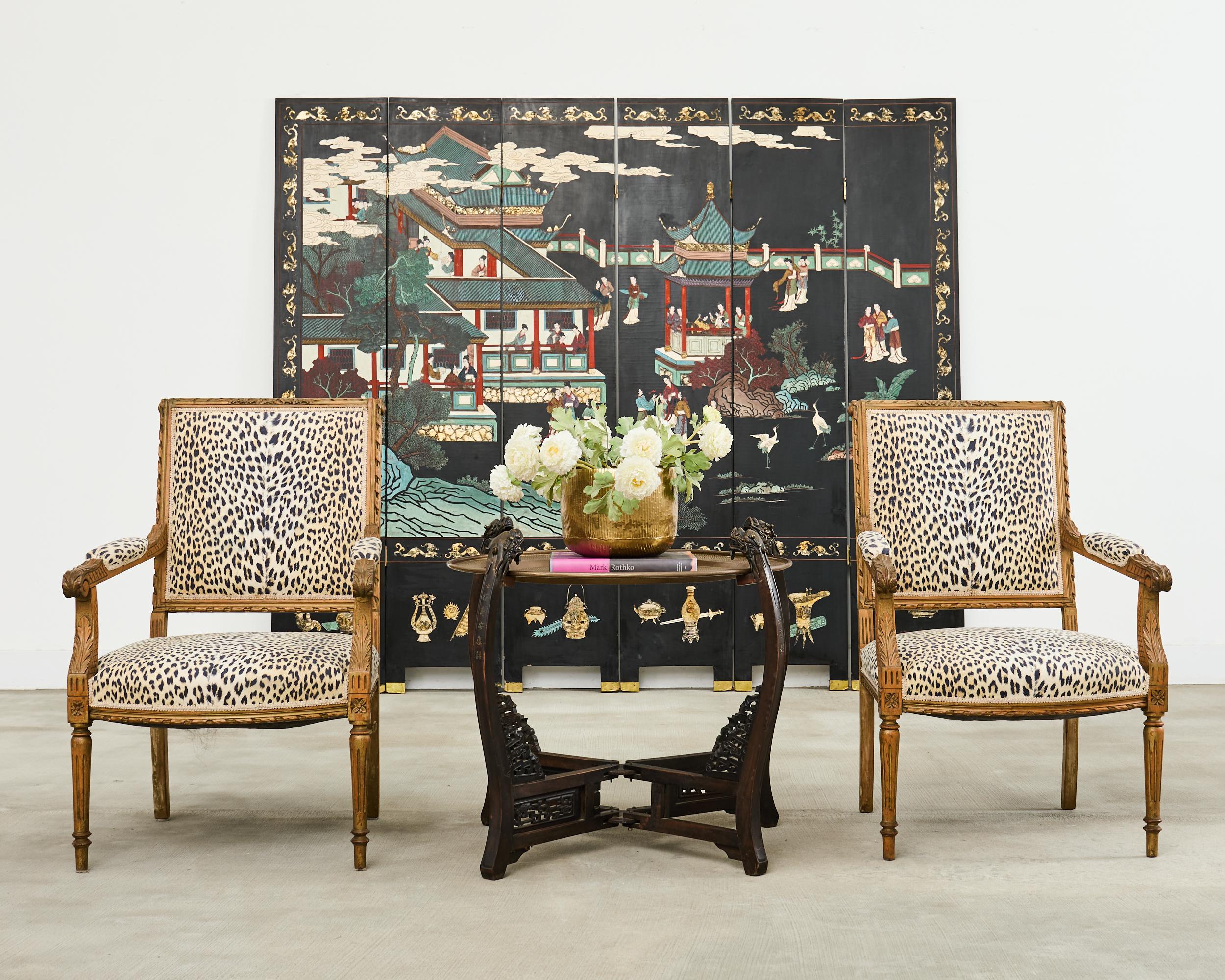 Dramatic pair of highly carved beechwood armchairs crafted in the grand French Louis XVI taste. The chairs feature a large square back with a scrolled crest decorated with floral detail. The generous seat is bowed in the front with large padded,