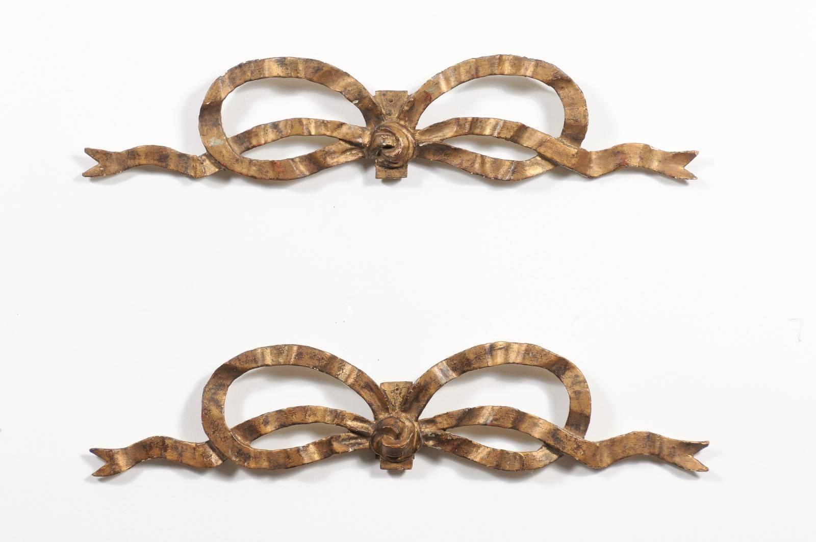 A pair of French Louis XVI style carved giltwood tied ribbon wall decorations from the early 20th century. Each of this French of French carved ribbons features an elongated shape, showing a delicate ribbon, typically found on Louis XVI mirrors or