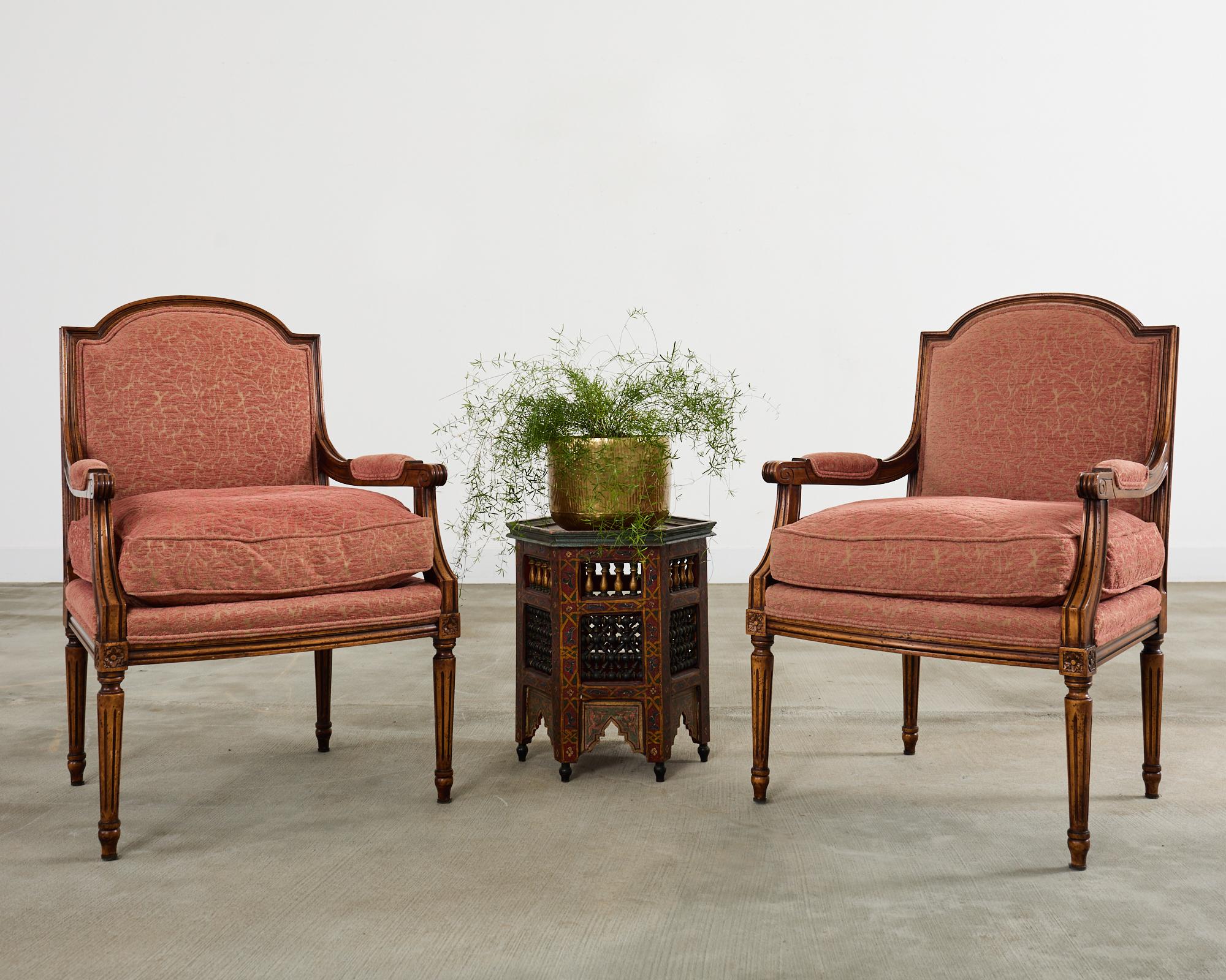 Opulenta coppia di poltrone fauteuil francesi in noce intagliato, realizzate secondo il gusto Luigi XVI. Le sedie presentano una cresta graziosamente arcuata e uno schienale quadrato con braccioli imbottiti. Le generose sedute sono dotate di un