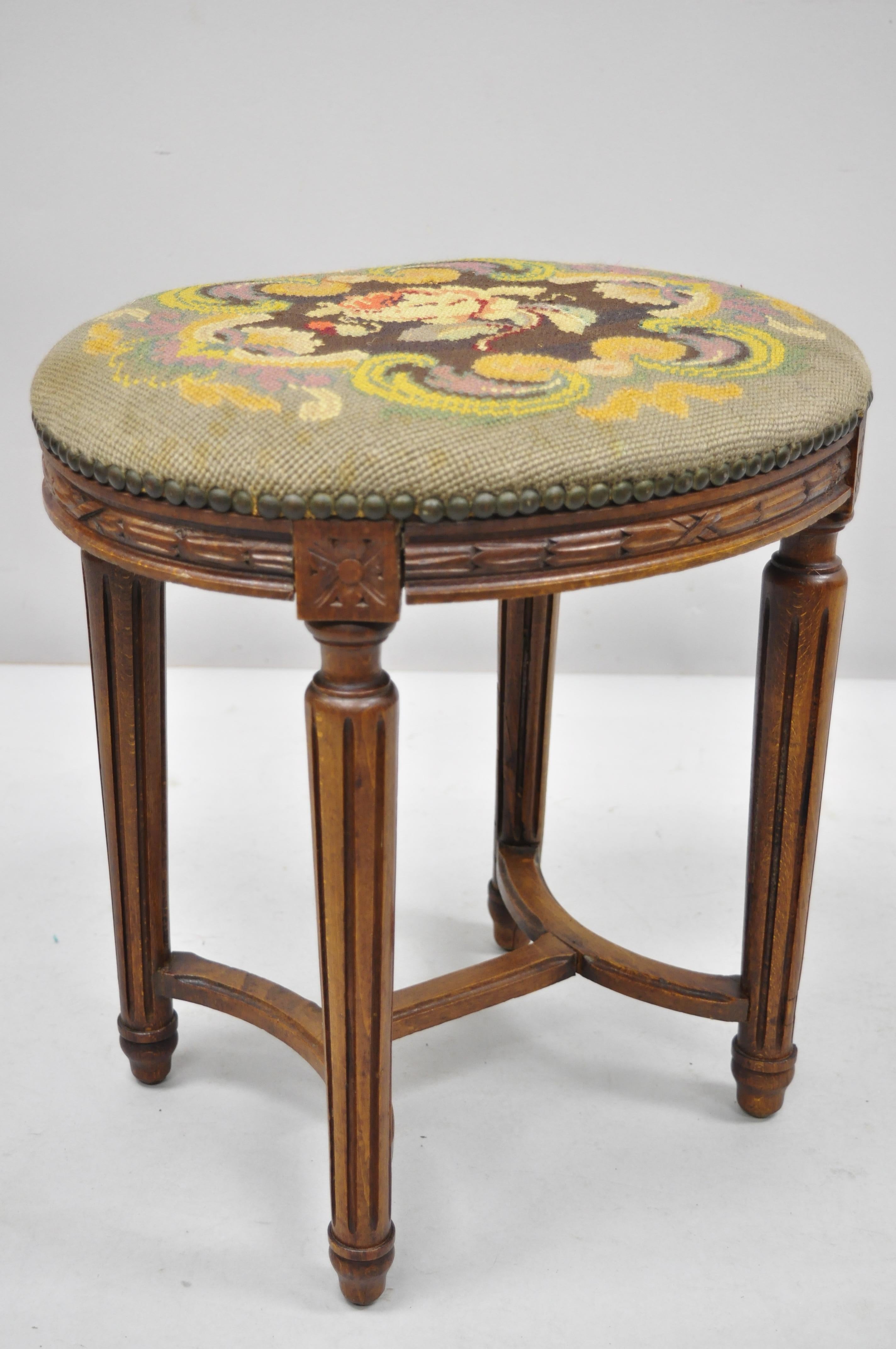 Pair of French Louis XVI style carved walnut and needlepoint oval stools. Item features floral needlepoint upholstery, remnants of label, solid wood frame, beautiful wood grain, tapered legs, very nice antique item, circa early 20th century.