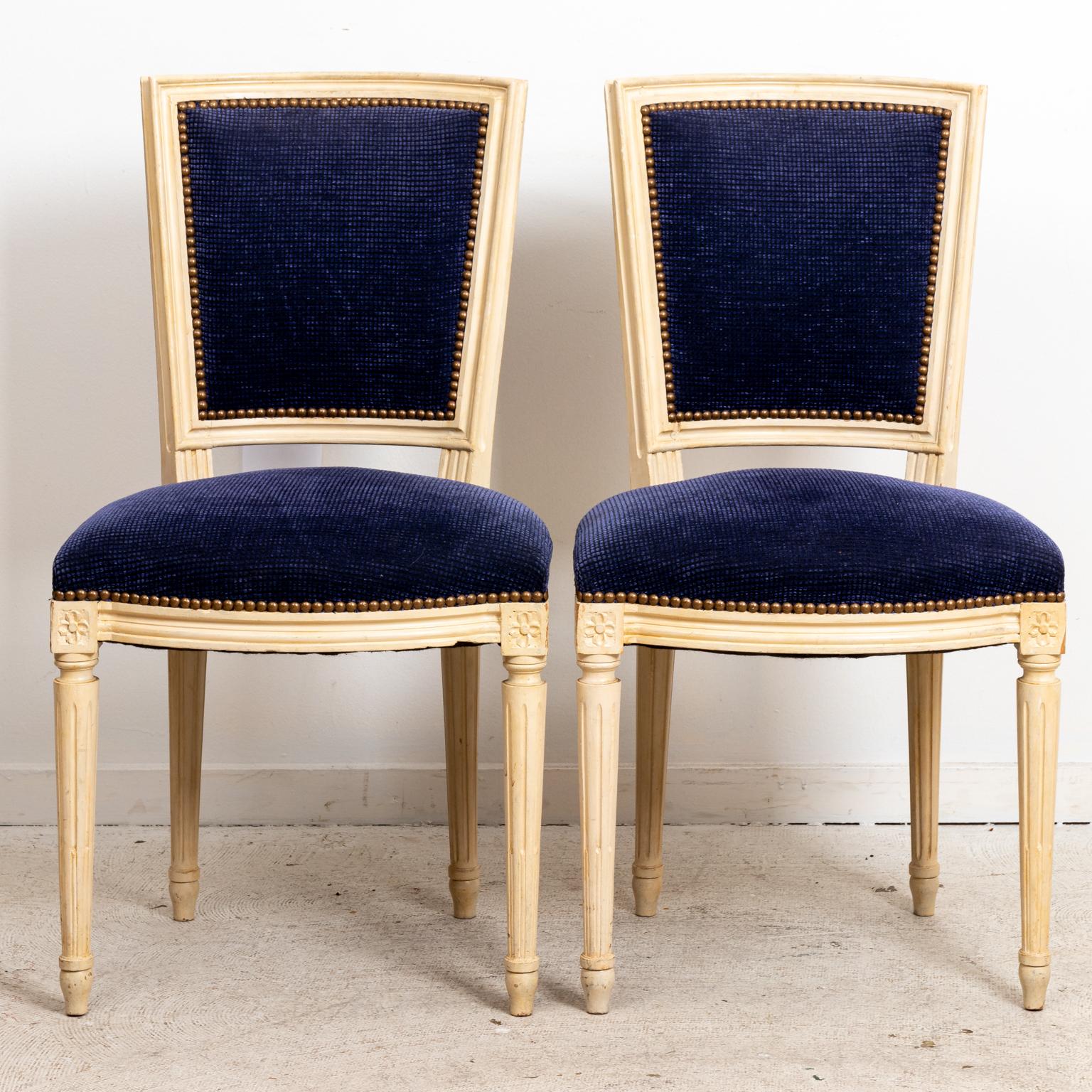 Circa 1940s pair of French Louis XVI style chairs with upholstered seat back and seat. The chair also features metal nail head trim and turned, fluted legs. Please note of wear consistent with age.