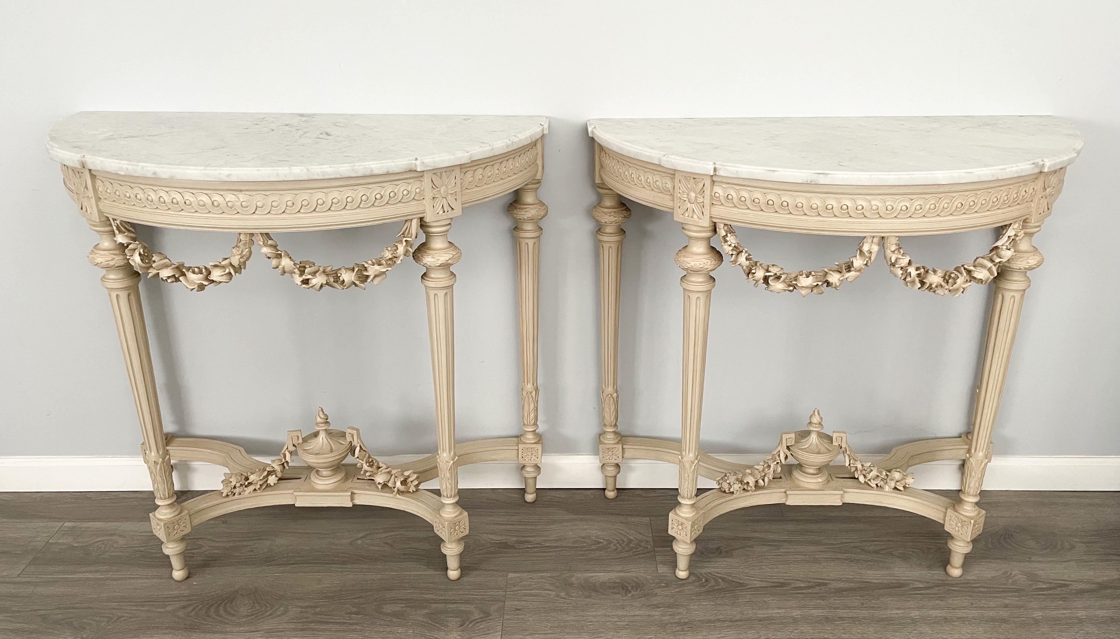 Glorious, pair of French, early 1900s Louis XVI-style console tables. 

 The tables feature carved solid wood bases with intricate decorations including garlands of flowers, urns, medallions and fluted tapered legs. Both tables retain their
