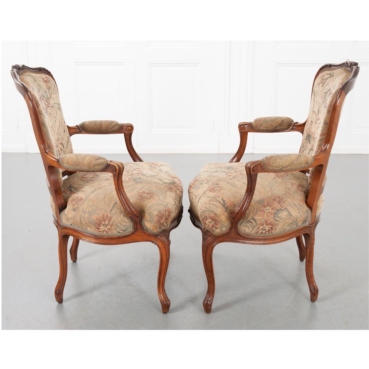 A lovely pair of French Louis XVI style carved walnut fauteuils are upholstered in a floral fabric with muted rose and green tones. The armchairs are beautifully carved and very comfortable. The seat height is 18”. C. 1900.