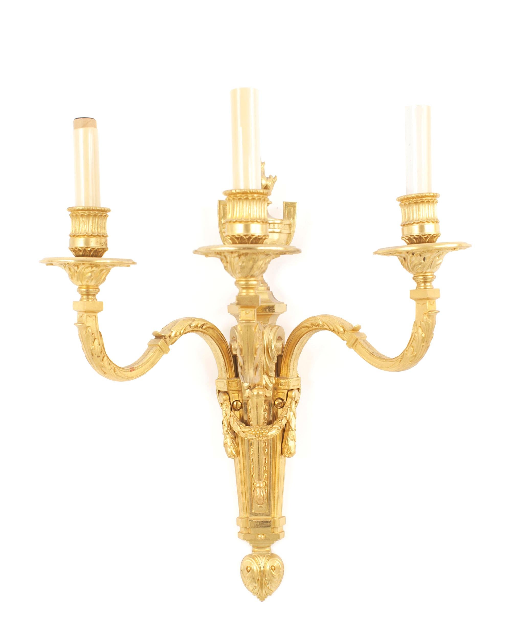 Pair of French Louis XVI style (19th Century) gilt wall sconces with three arms, urn and flame design tops, and swag centers. (PRICED AS Pair)
