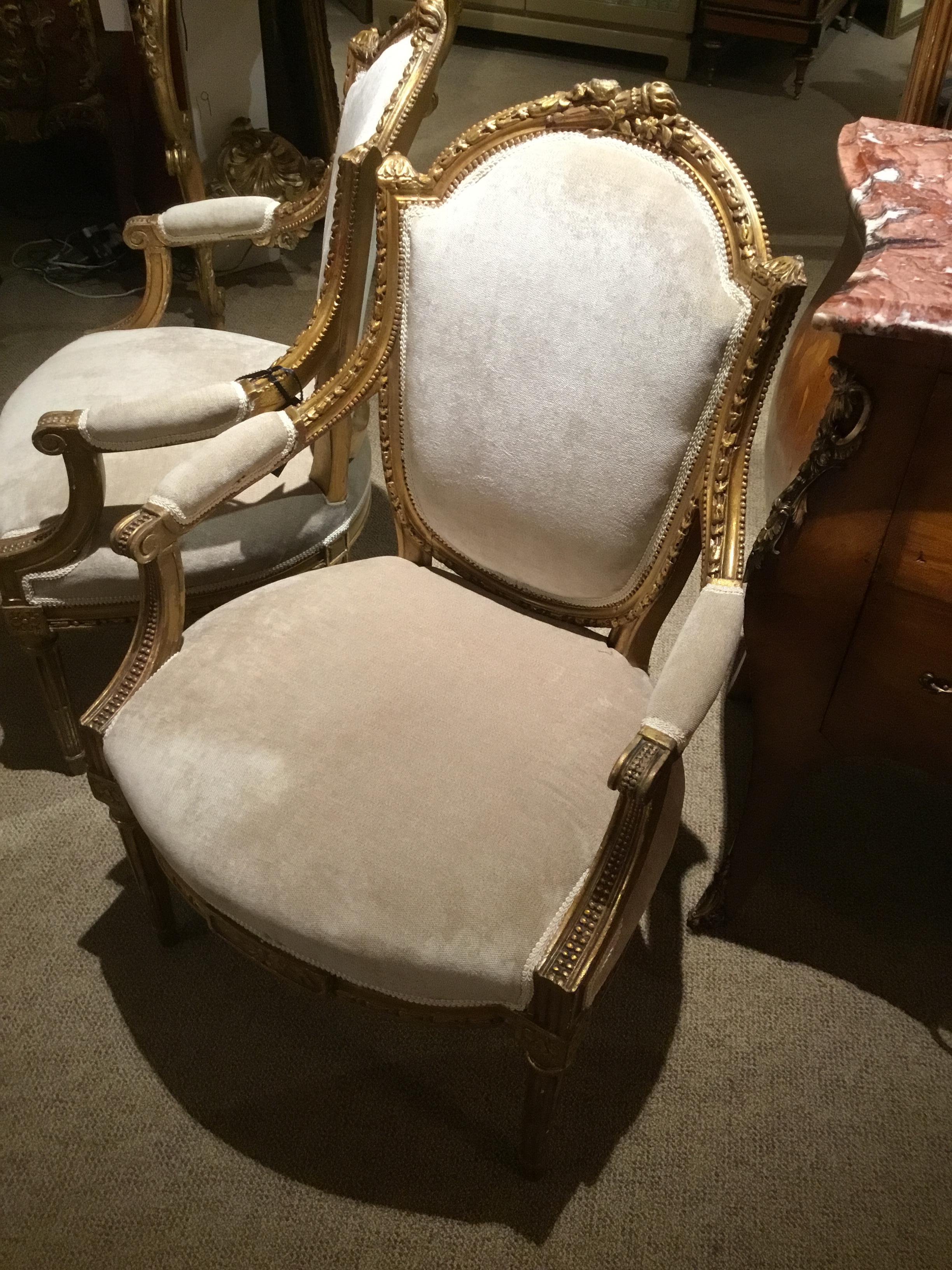 French Louis XVI style giltwood chairs with a flamed torch and foliate 
Design at the crest of these chairs. A carved and reeded leg is featured.