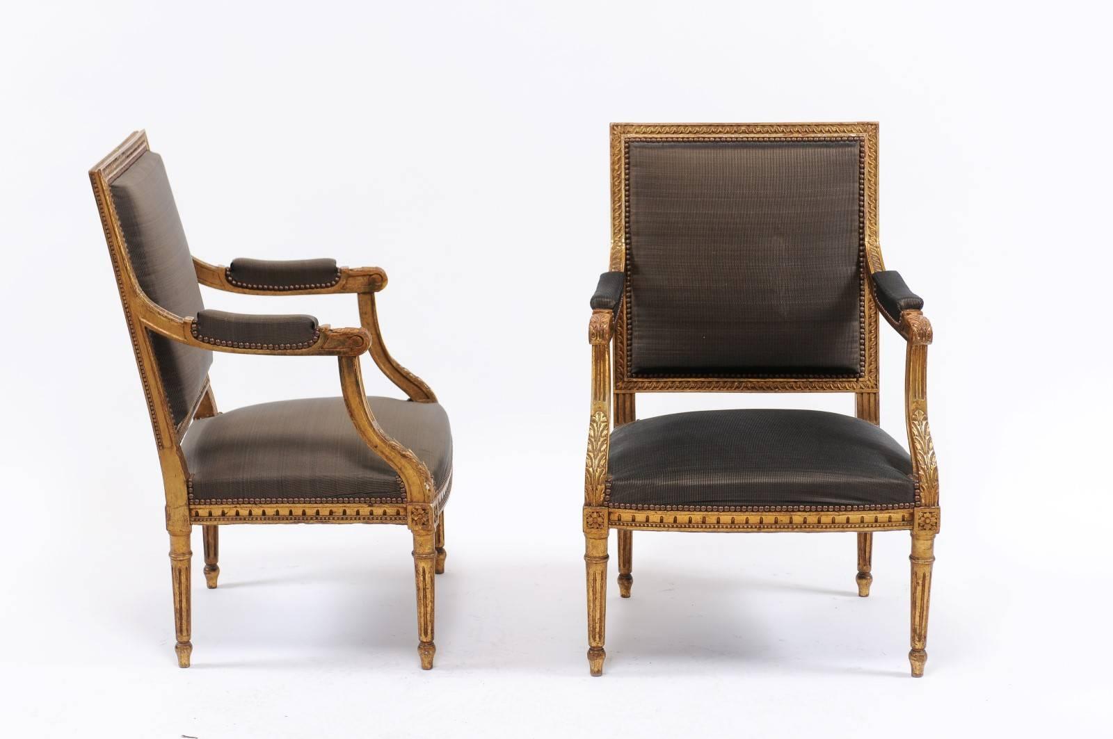 A pair of French giltwood upholstered armchairs of Louis XVI style with acanthus leaves carving, beaded molding, rosettes and fluted legs from the late 19th century. We flipped over this pair of Louis XVI-style armchairs, circa the late 19th