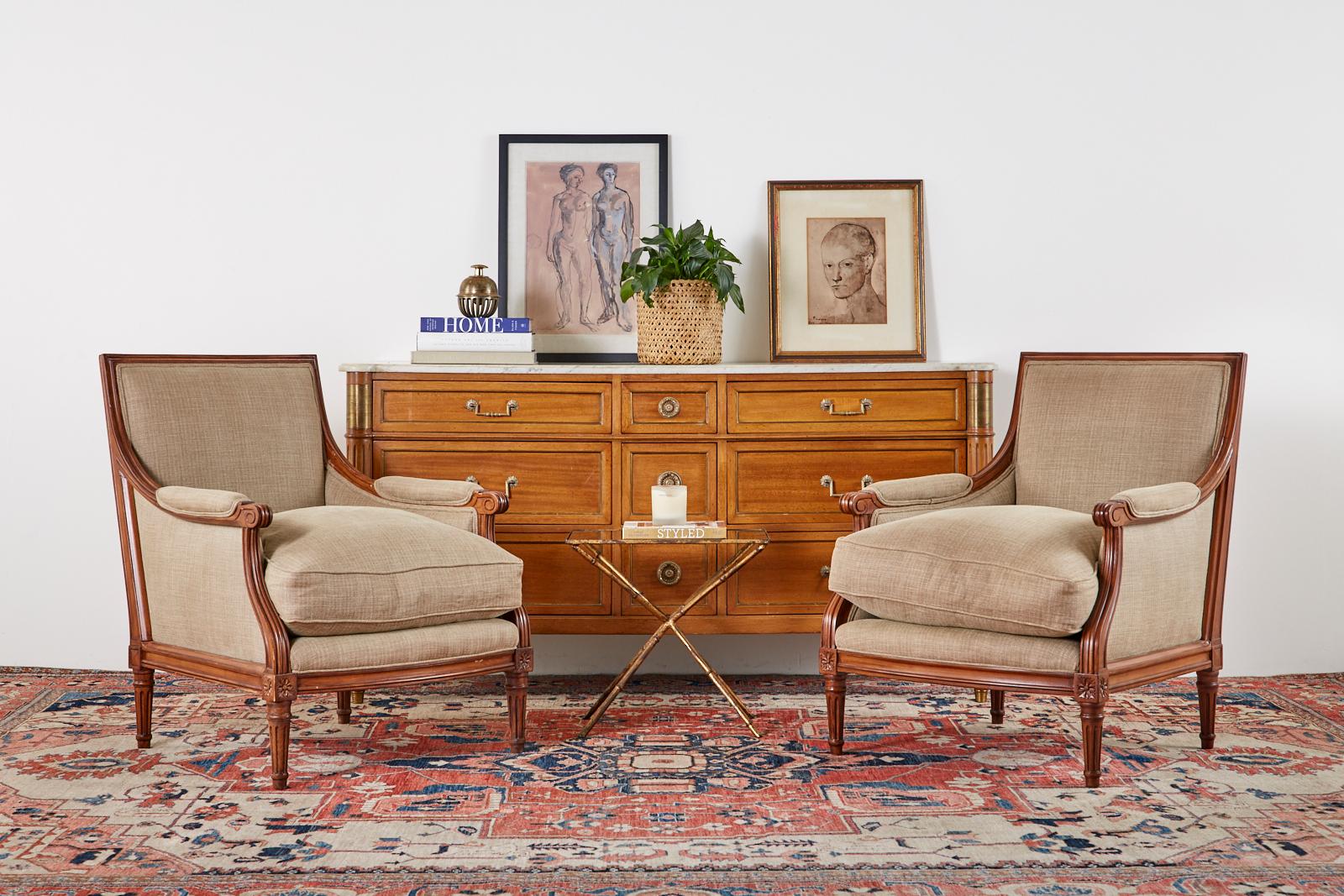 Impressive pair of mahogany bergère armchairs made in the grand French Louis XVI taste. The bespoke pair of chairs feature a large, generous mahogany frame with a long seat. The backs of the chairs are squared and have graceful curved padded arms