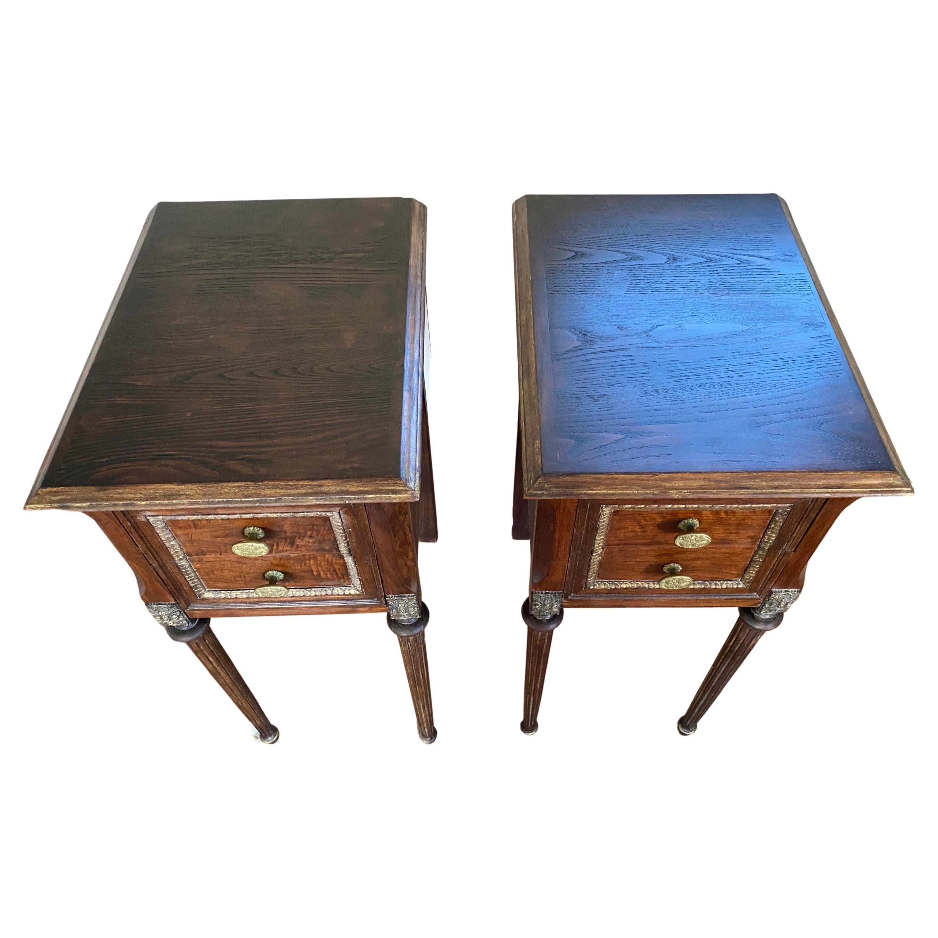 A pair of smart Louis XVI style nightstands or bedside end tables with gilded decorative accents. The stands each have two drawer with brass knobs top. The gold toned accents adds extra style and elegance to these stands.

 