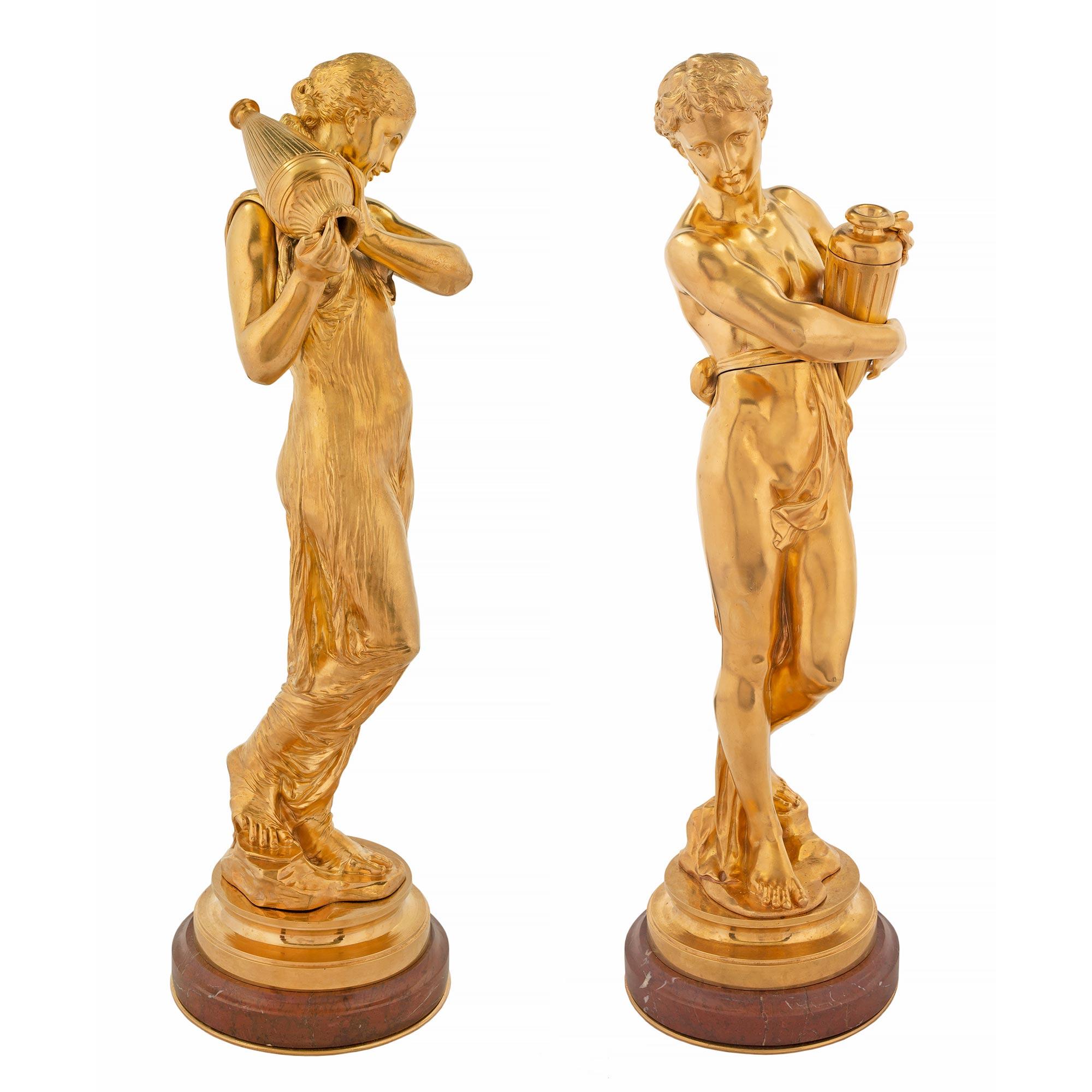 A very handsome and high quality pair of French Louis XVI st. ormolu and Rouge Griotte marble statues. Each is raised by an ormolu bottom plate below the mottled edge circular Rouge Griotte marble base. One figure is of a young maiden dressed in