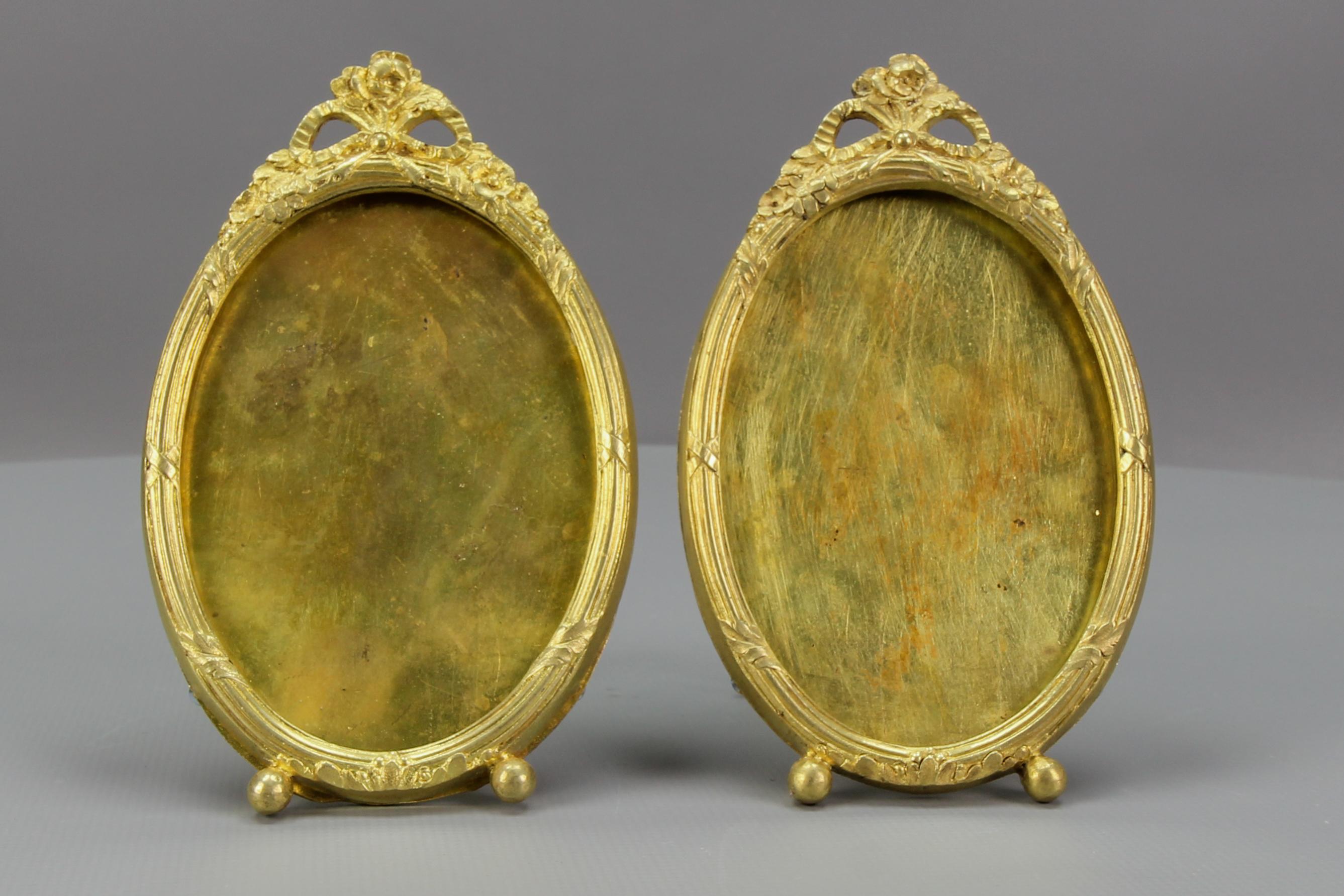 A pair of French Louis XVI-style oval bronze photo or picture desktop easel frames from circa the 1900s.
This adorable pair of picture frames is made of bronze and brass and has an easel supporting leg on the back. Decorated with flowers and a bow