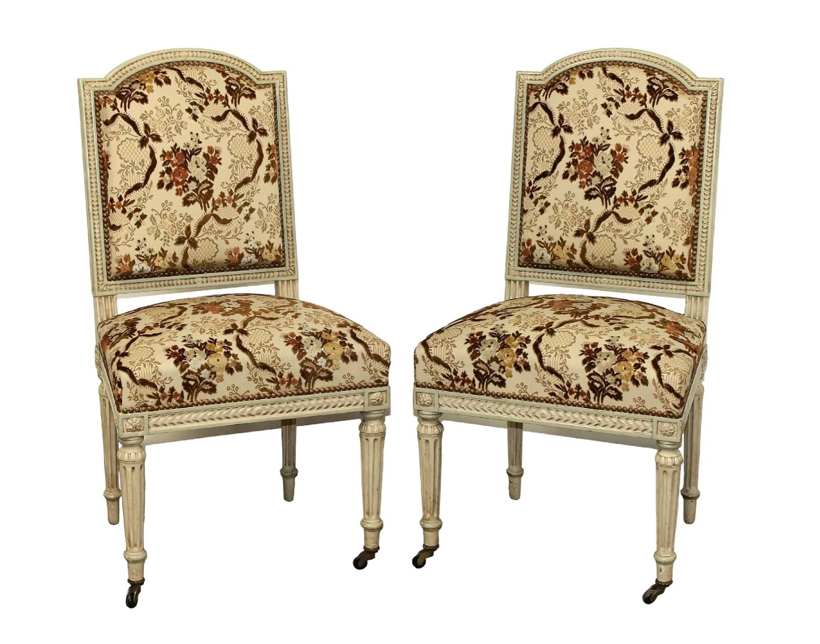 Pair of French Louis XVI style painted side chairs on fluted legs. Seats and backs are upholstered in a brown/tan/cream floral fabric with cut velvet details, in very nice condition. Brass nail heads border the upholstery; casters on the front legs.