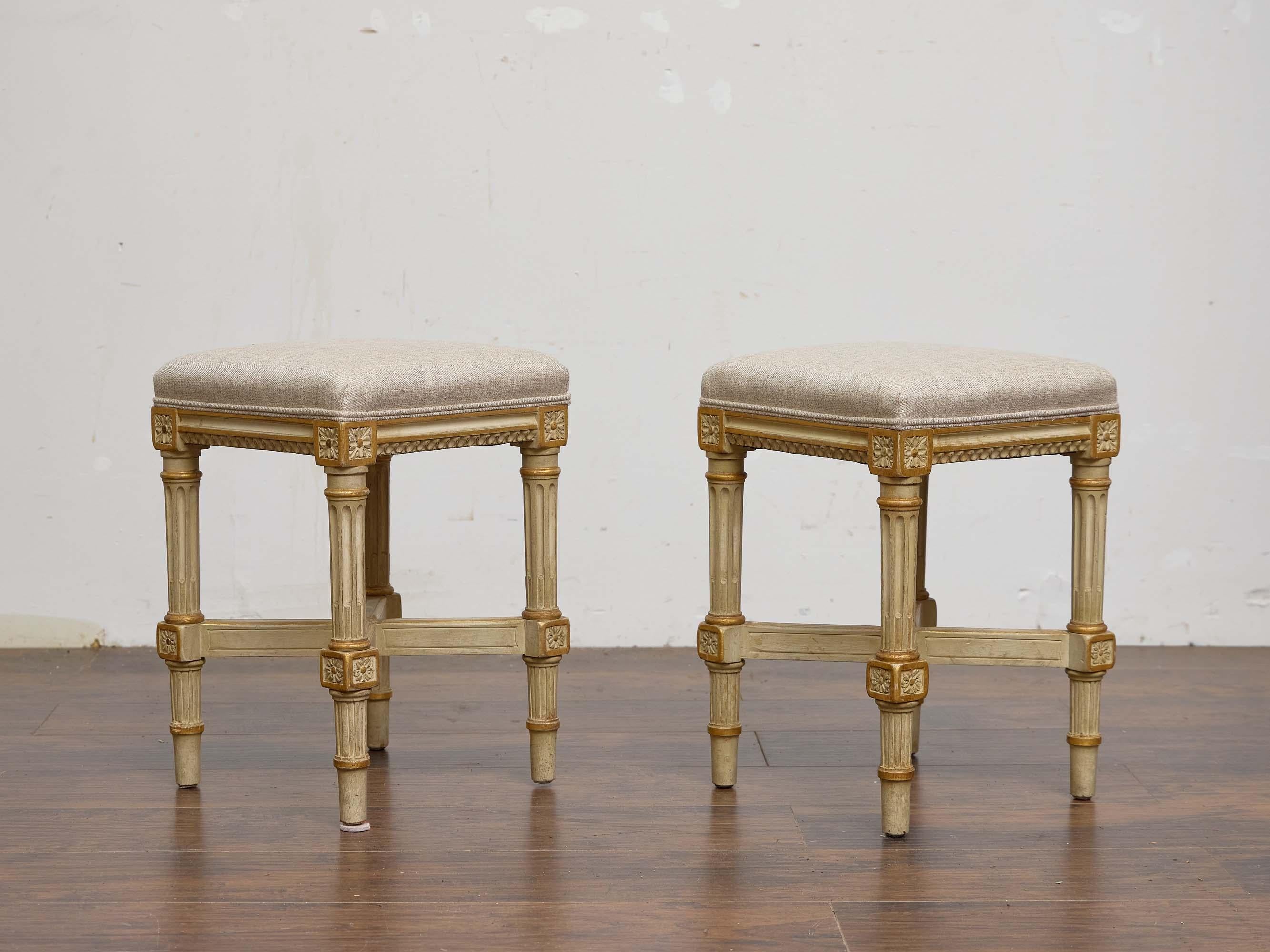 This charming pair of French stools dates to the 1920s and reflects the refined elegance of the Louis XVI style. Each stool features fluted, tapering legs joined by an X-form stretcher, enhancing stability while adding visual interest. The carved