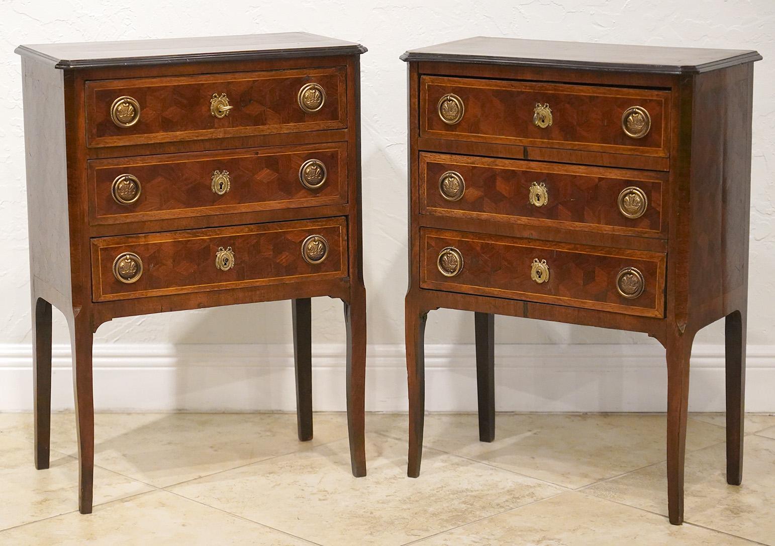 This pair of elegant French Louis XVI style parquetry commodes dating to the early 20th century feature banded inlaid tops with ebonized trim above three banded parquetry drawers and sides resting on slightly shaped tapering legs.