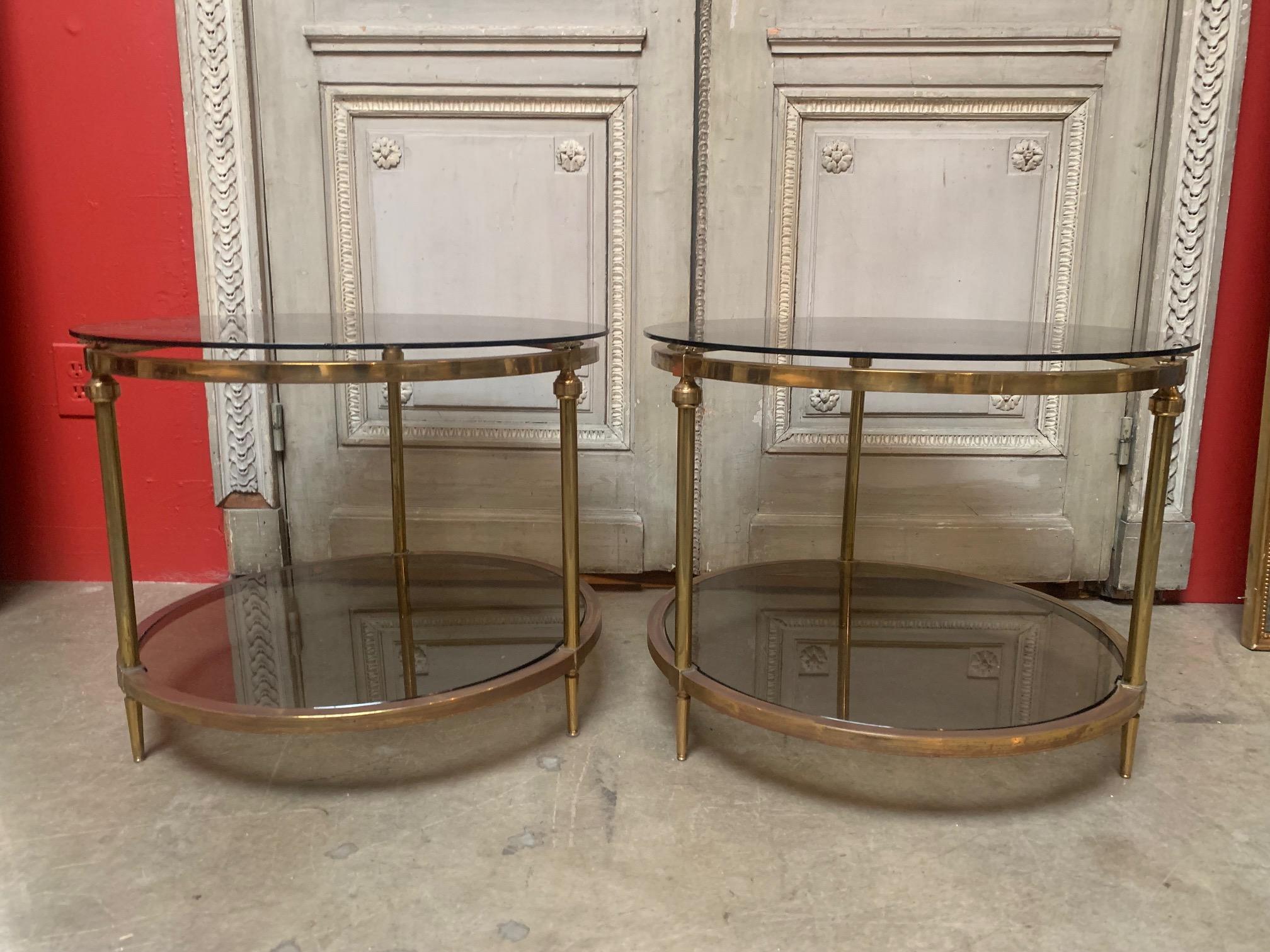 A pair of French 20th century round two tiered brass and smoked glass end tables in a neoclassical style. Great scale and function.