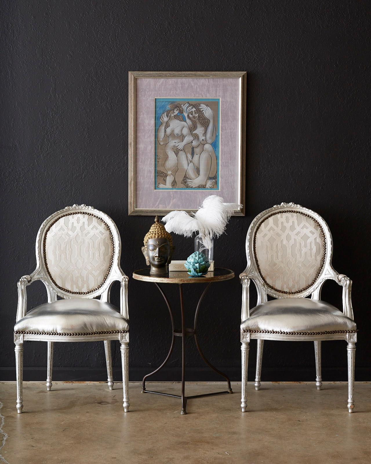 Dazzling pair of French armchairs featuring carved Louis XVI style frames that have been painstakingly silver leaf finished by hand. The frames have been upholstered with a matching silver metallic fabric on the seat and a Schumacher style geometric